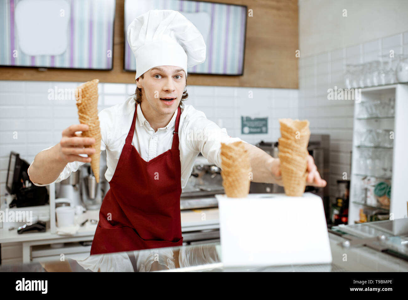 Stattliche Verkäufer in Schürze und Mütze, Waffeln und Eis in der modernen Konditorei Stockfoto