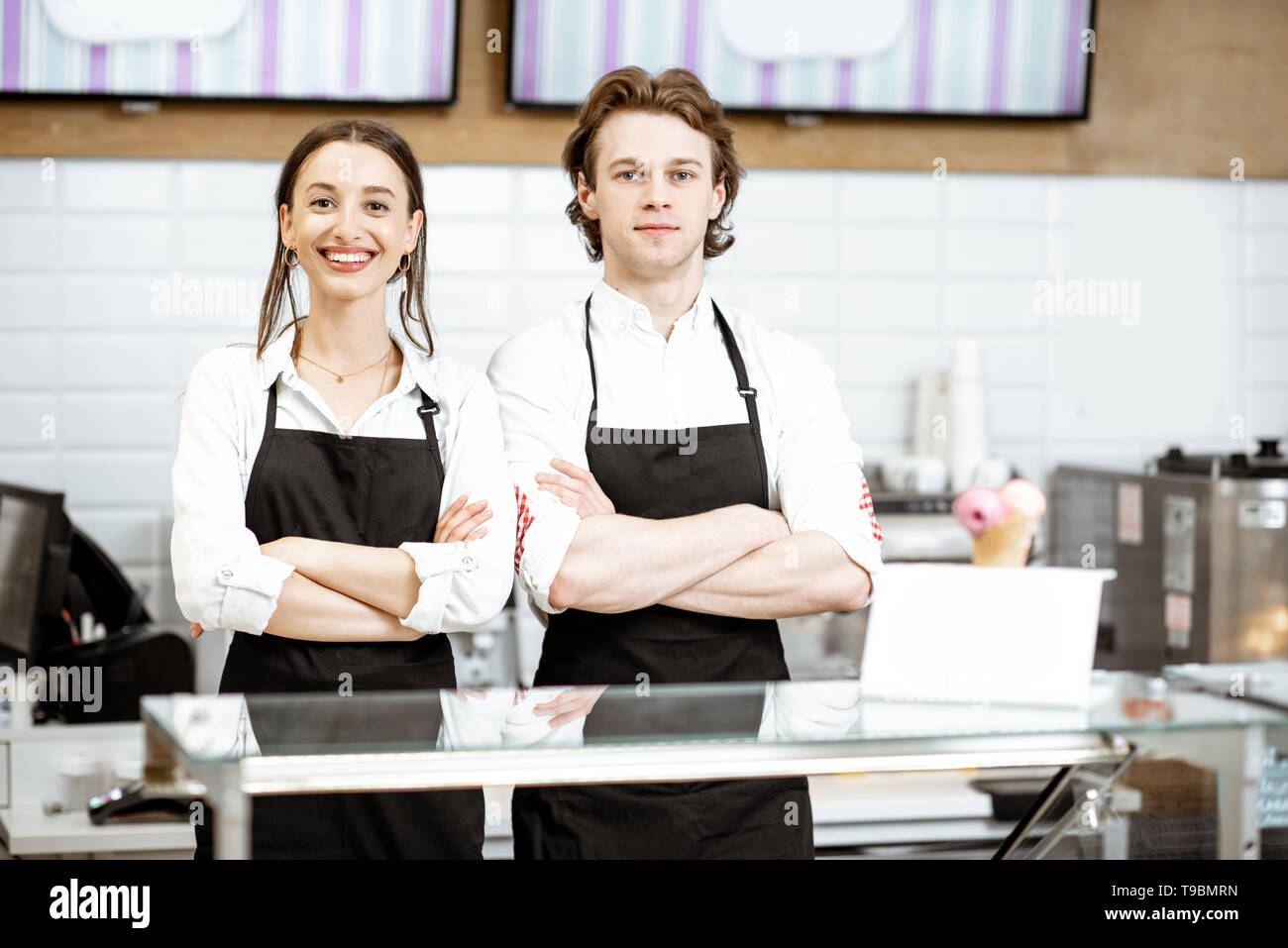Porträt eines Mannes und einer Frau im schwarzen Schürzen zusammen als Verkäufer in der modernen Konditorei und Café Stockfoto
