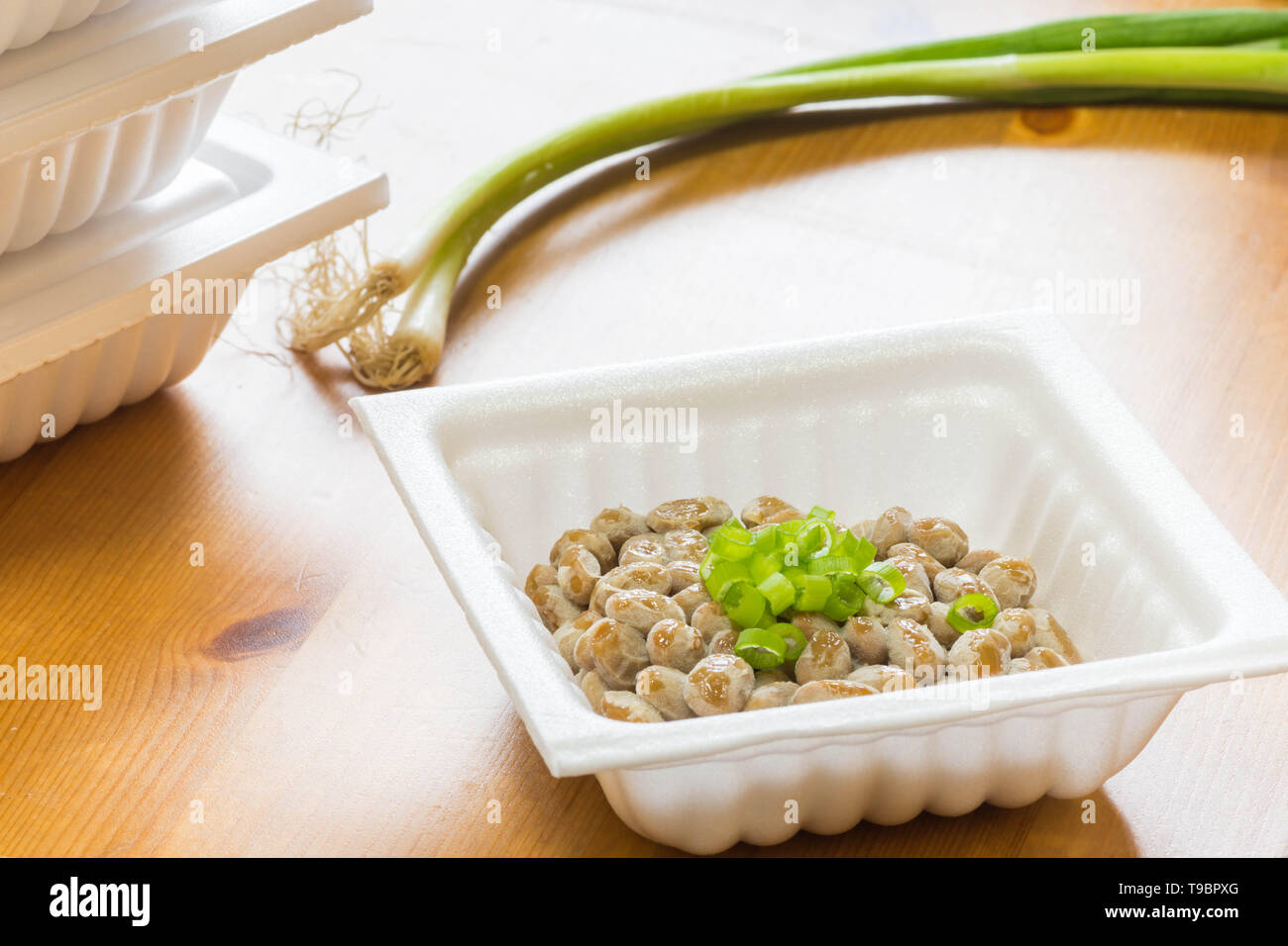 Natto - eine beliebte und gesunde Japanische Lebensmittel aus vergorenem Bohnen in einem Styropor Behälter mit grünen Frühlingszwiebeln als Belag. Stockfoto