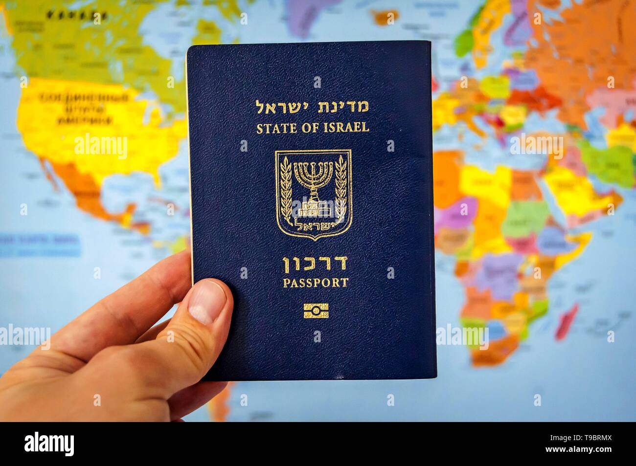 Hand, die den Pass des Staates Israel gegen die bunte Welt Karte Atlas. Israel die israelische Staatsbürgerschaft Konzept, biometrische "arkon 'Pass Stockfoto