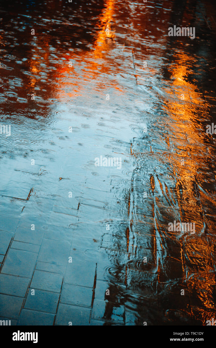 Abstrakte Fotografie von Regen. Regentropfen auf Asphalt im Abendlicht leuchten. Stockfoto