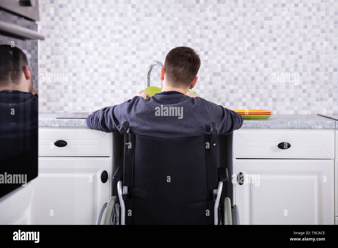 Behinderte Mann sitzt auf Rollstuhl Waschen und Reinigung Geschirr in der Küche Stockfoto