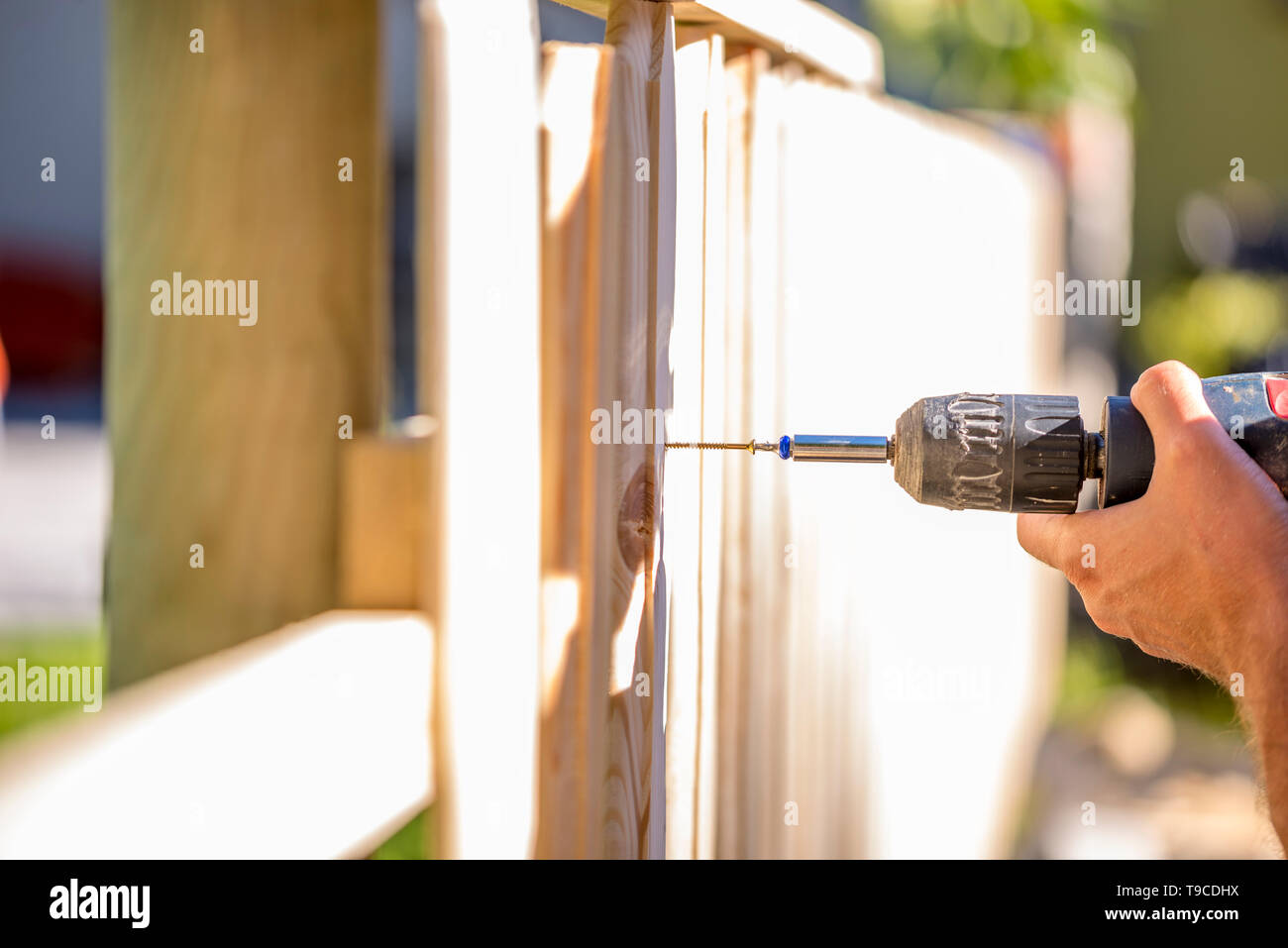 Menschen Sie errichten einen hölzernen Zaun im Freien mit einem handheld elektrischen Bohrer, Bohrer ein Loch Anhängen eine aufrechte Plank, Nahaufnahme von seiner Hand und das Werkzeug in Stockfoto