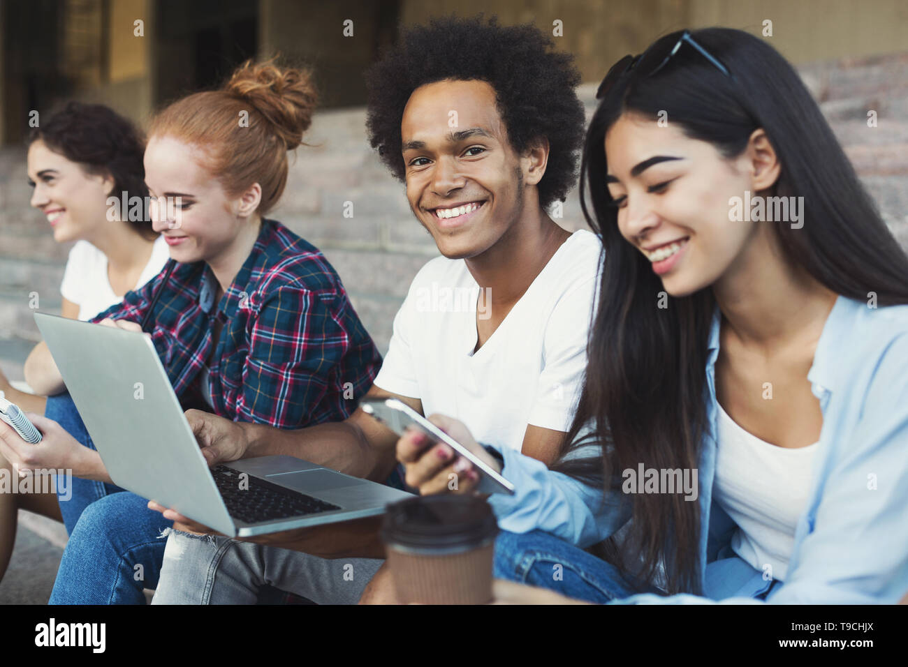 Schwarzer Mann mit Laptop lächelnd an Kamera, Zeit mit Freunden Stockfoto