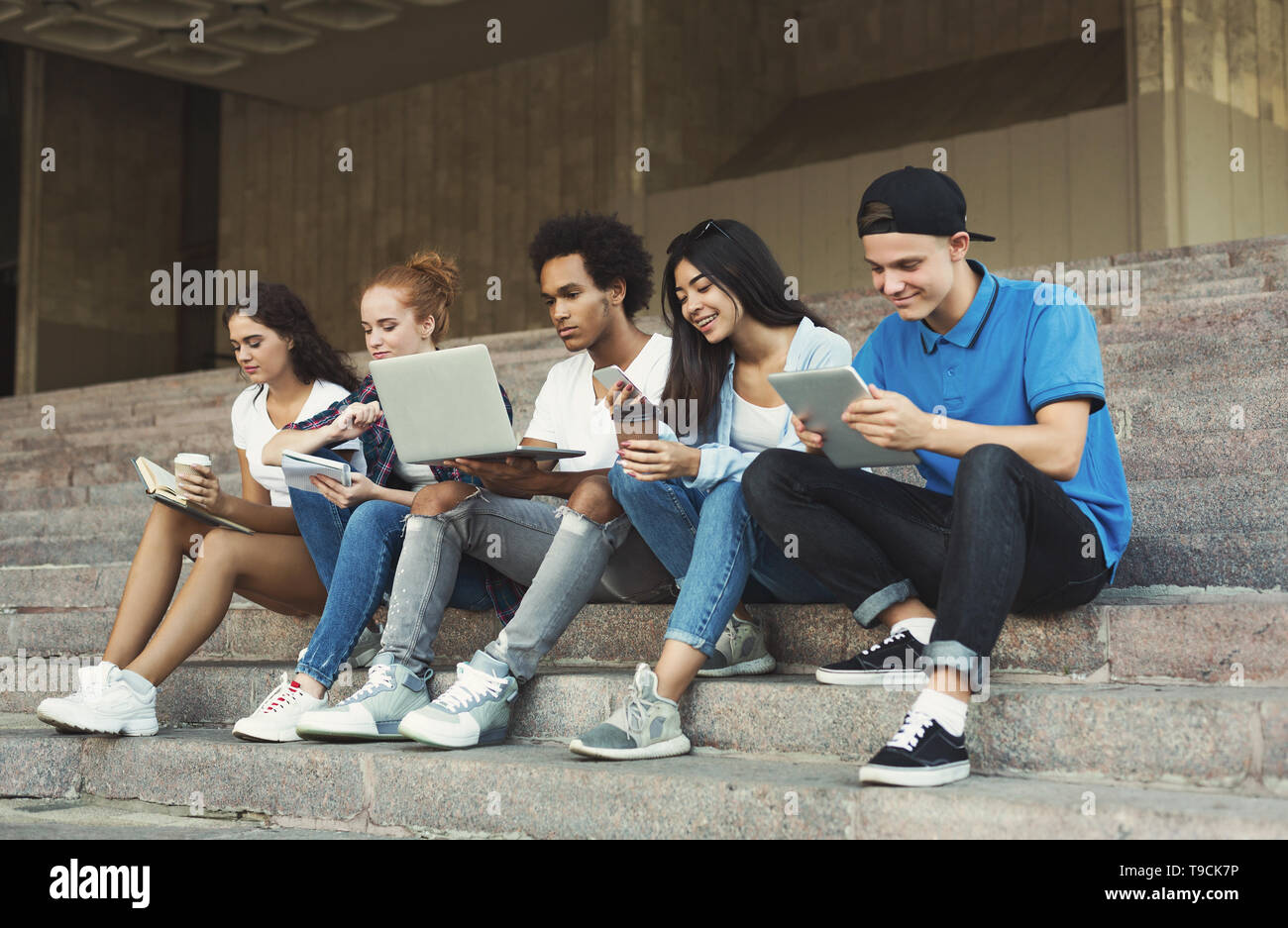 Gruppe von verschiedenen Jugendlichen mit Gadgets, sitzen auf der Treppe im Freien Stockfoto