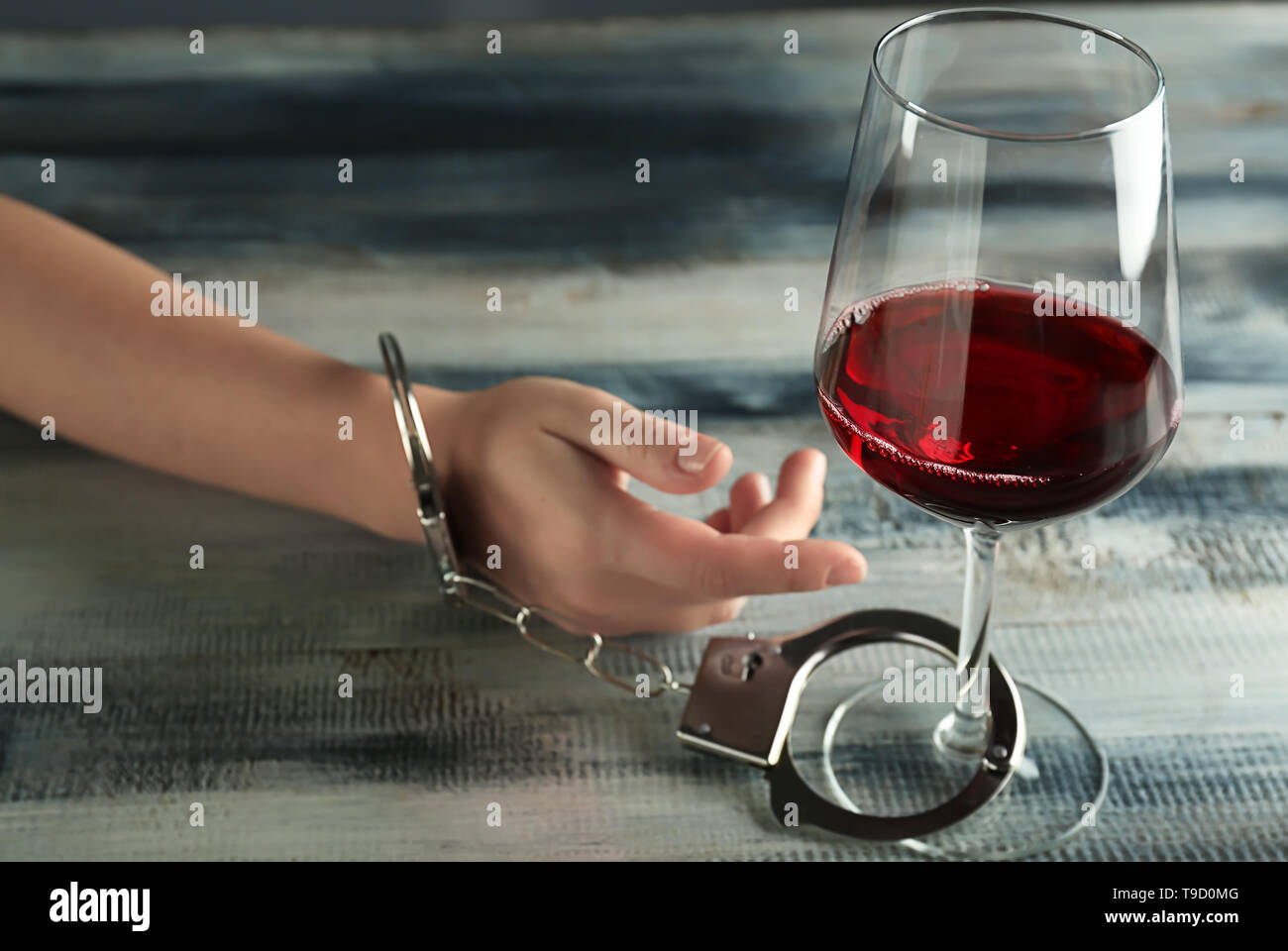 Frau in Handschellen zu Glas Wein auf Holztisch. Konzept des Alkoholismus Stockfoto