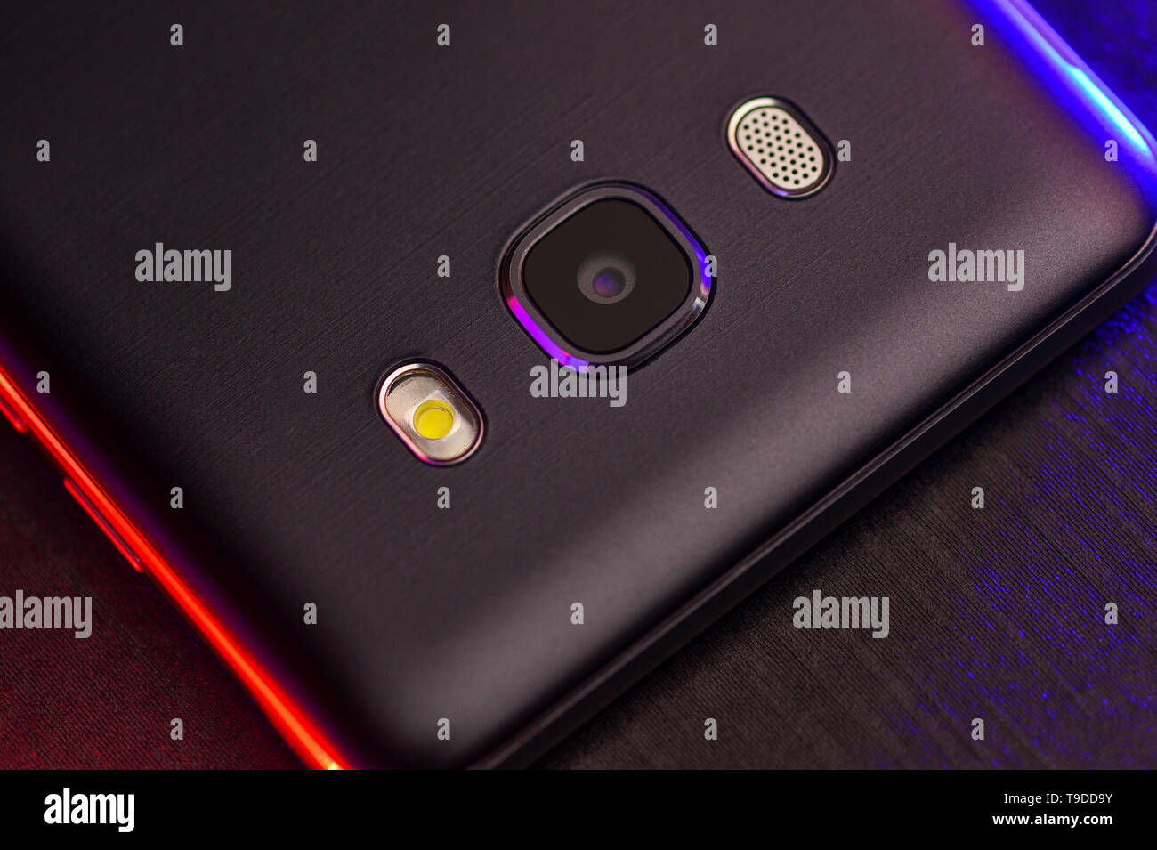 Ein Fragment der Cell Phone Case in Schwarz mit roten und blauen Hintergrundbeleuchtung. Das Telefon liegt auf dem Schwarzen technologische Oberfläche der Kamera mit Blau. Stockfoto