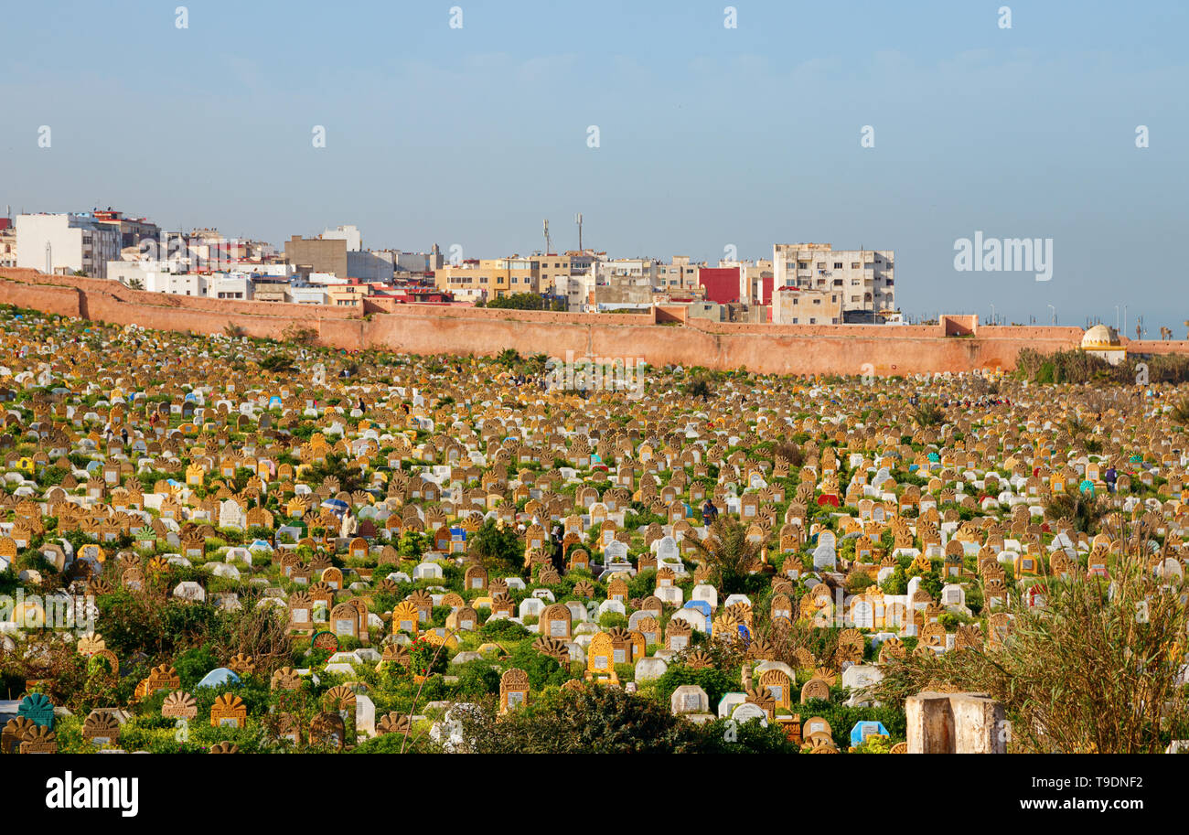 Friedhof mit Gräbern und Grabsteinen, mit Gras an der Küste bedeckt mit Wohnbauten im Hintergrund an einem sonnigen Nachmittag. Rabat, Marokko. Stockfoto