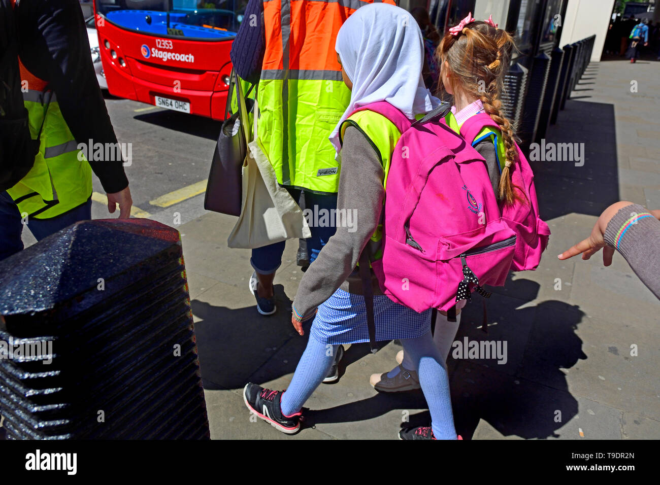 London, England, UK. Gruppe von Schulkindern warten auf einen Bus - ein muslimisches Mädchen mit Kopftuch zu erhalten Stockfoto