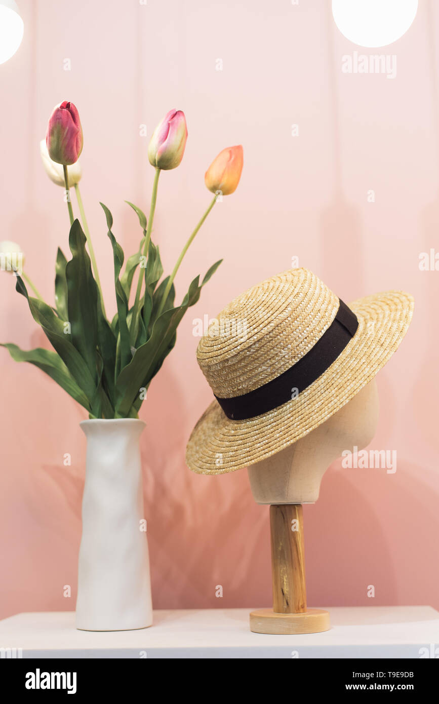 Schaufensterpuppe Kopf im Stroh Hut auf Schaufenster. Hut in der Mall auf ein Pastell rosa Hintergrund neben Tulpen in der Vase Stockfoto