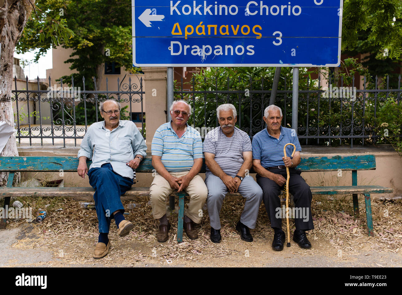 Vier griechischen Männer sitzen auf einer Bank durch die Dorfkirche in Kefalas in Kreta unter ein Schild zu Drapanos und Kokkino Chorio Stockfoto