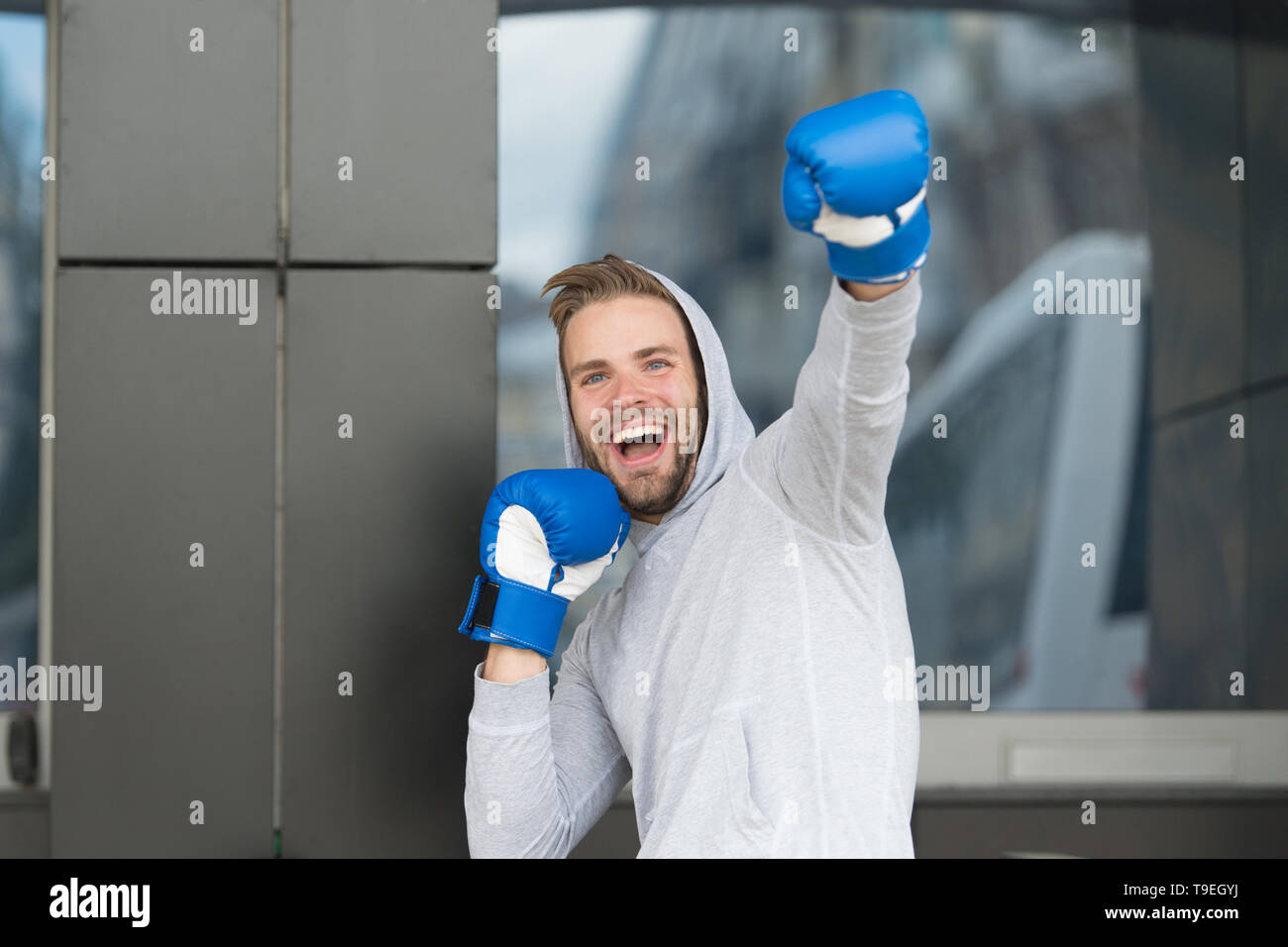 Sieger nimmt sie alle. Mann auf lächelnde Gesicht mit Boxhandschuhen als Sieger posiert, im städtischen Hintergrund. Sportler feiert den Sieg. Erfolg Konzept. Mann Mot Stockfoto