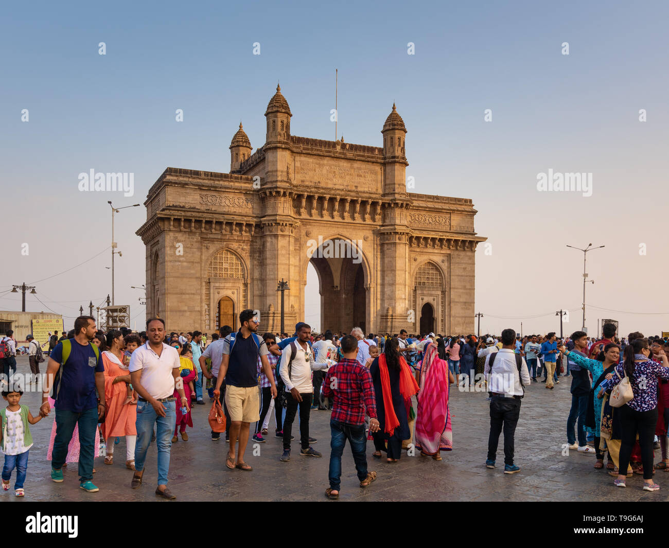 Menschenmassen von Touristen, die an einem klaren Tag in Mumbai am großen Steinbogen des Gateway-of-India-Denkmals vorbeigehen. Berühmtes Wahrzeichen-Außenbild. Stockfoto
