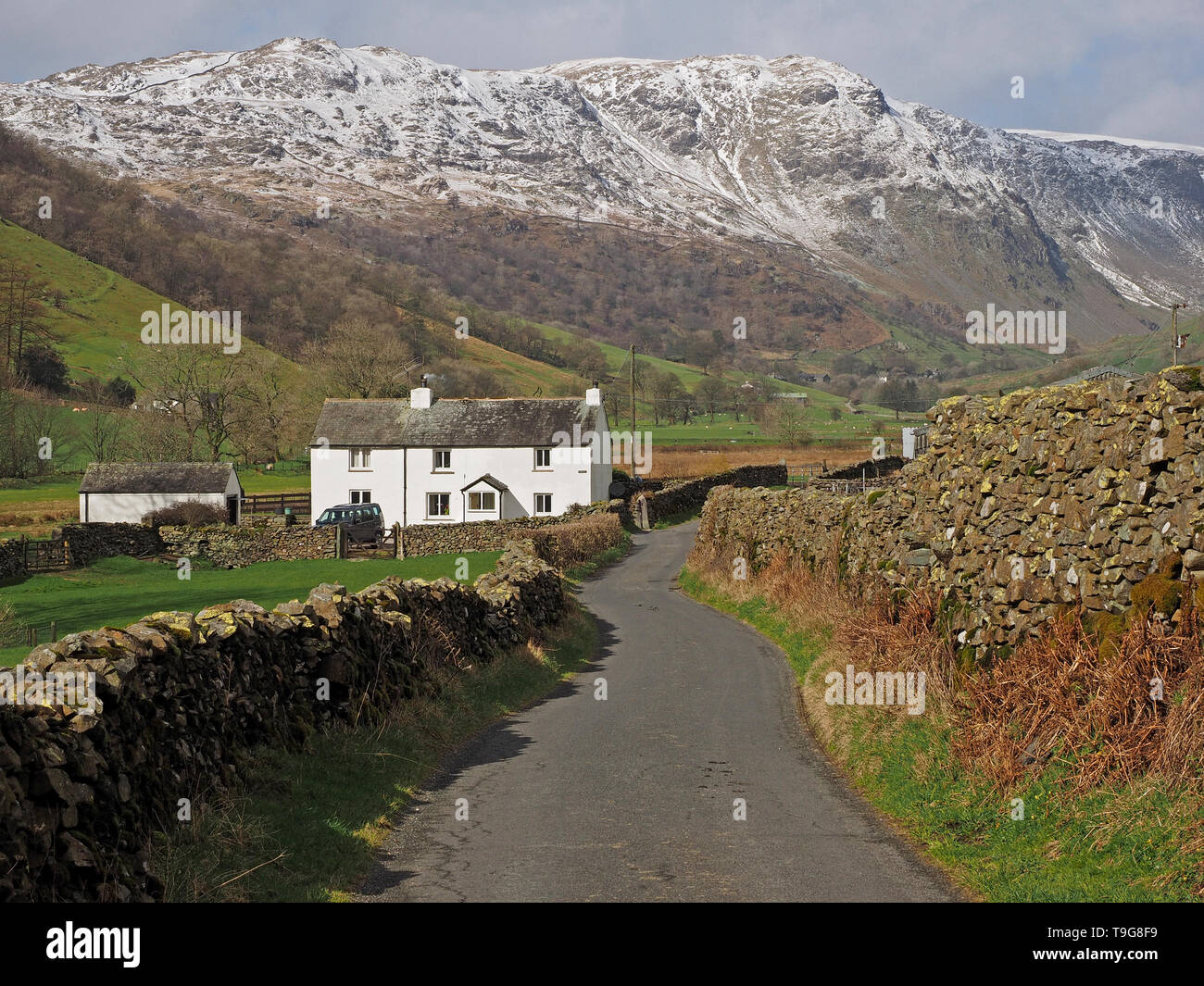 Landschaft in Long Sleddale Cumbria, England, Großbritannien mit weißem Farmgebäude, Trockenmauern, gewundener Gasse und Schnee auf fernen Hügeln Stockfoto