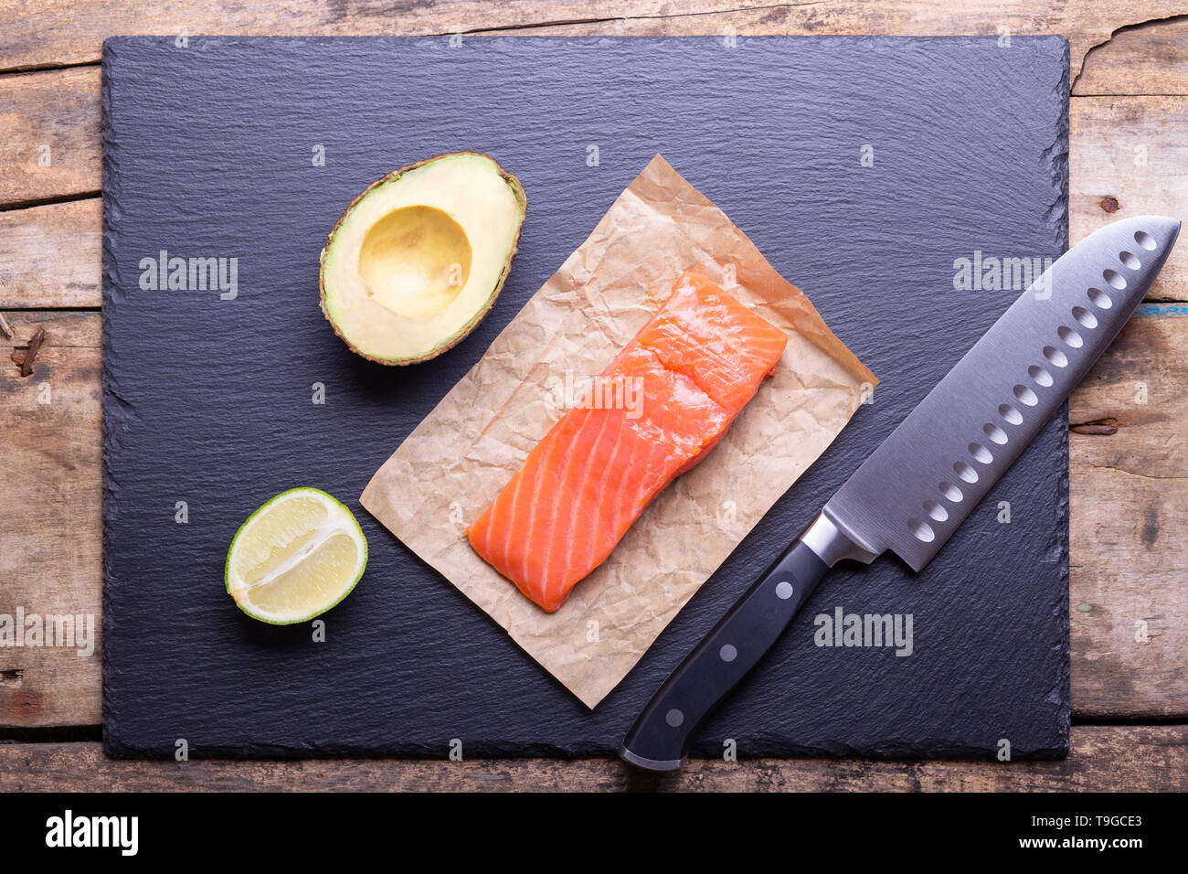 Flache Layout der Lachsfilet mit Avocado, Kalk und großen Messer auf schwarzem Schiefer Hintergrund Stockfoto