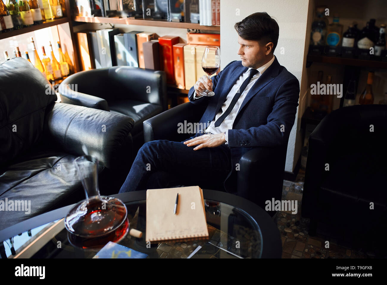 Jungen gutaussehenden Mann auf Stuhl Verkostung cognac sitzen. Bis schließen Seitenansicht Foto. Entspannung Konzept Stockfoto