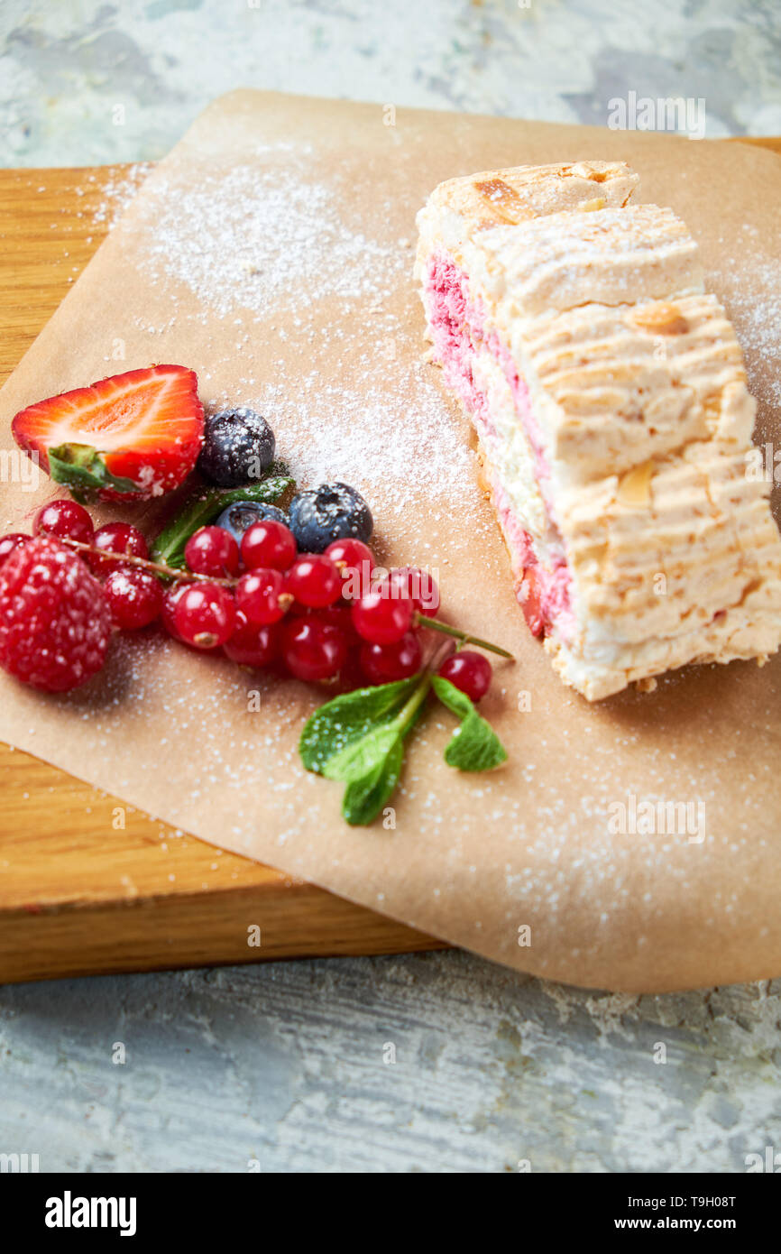 Baiser roll ist mit Beeren auf einem holzbrett eingerichtet. Grau strukturierten Hintergrund. Schöne Gerichte. Nachtisch. Lebensmittelkette Stockfoto