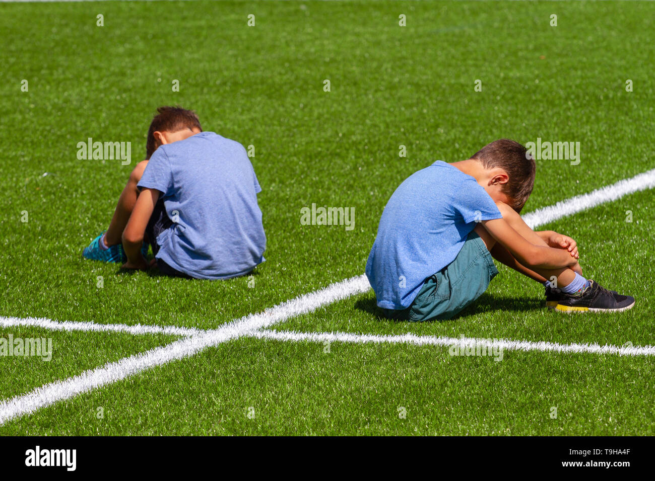 Bildung, Mobbing, Konflikt, soziale Beziehungen und Personen Konzept - Zwei traurig enttäuscht Jungs Rücken an Rücken sitzen auf dem Rasen im Stadion Feld Stockfoto