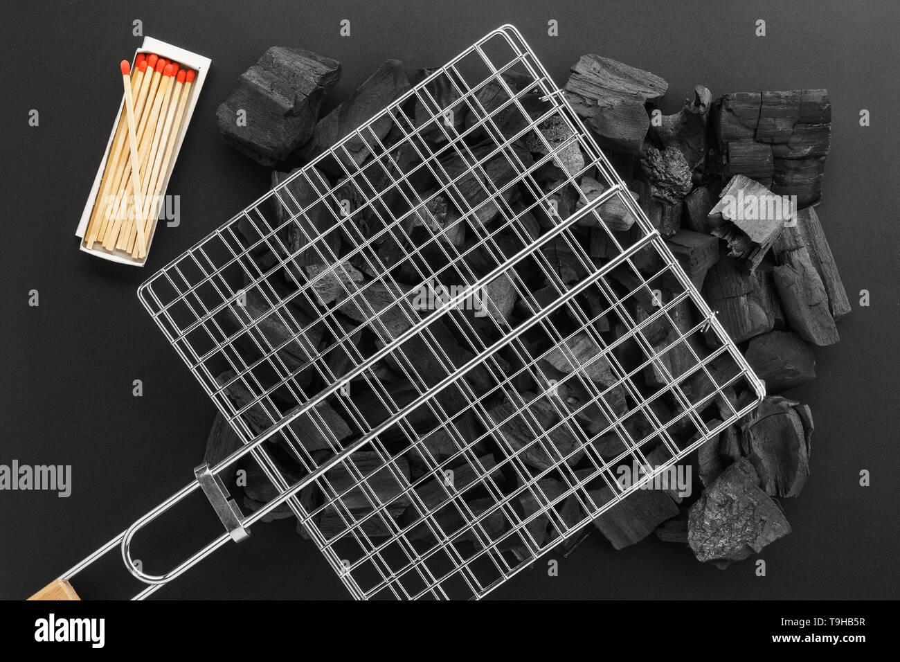 Grill Gitter auf Holzkohle Stücke und eine Schachtel Streichhölzer. BBQ-Vorbereitung gesetzt. Schwarzen Hintergrund. Flach. Stockfoto