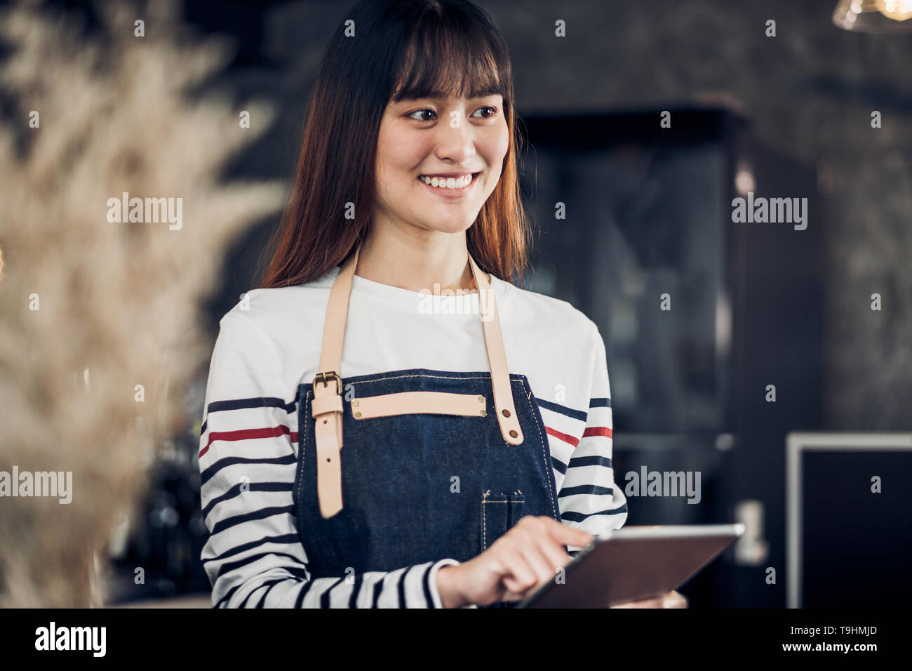 Asiatische Frau barista Schürze tragen halten Tablet Computer/Menü mit lächelnden Gesicht im Cafe warten um von Kunden, Kaffee Business Owner Konzept. Stockfoto
