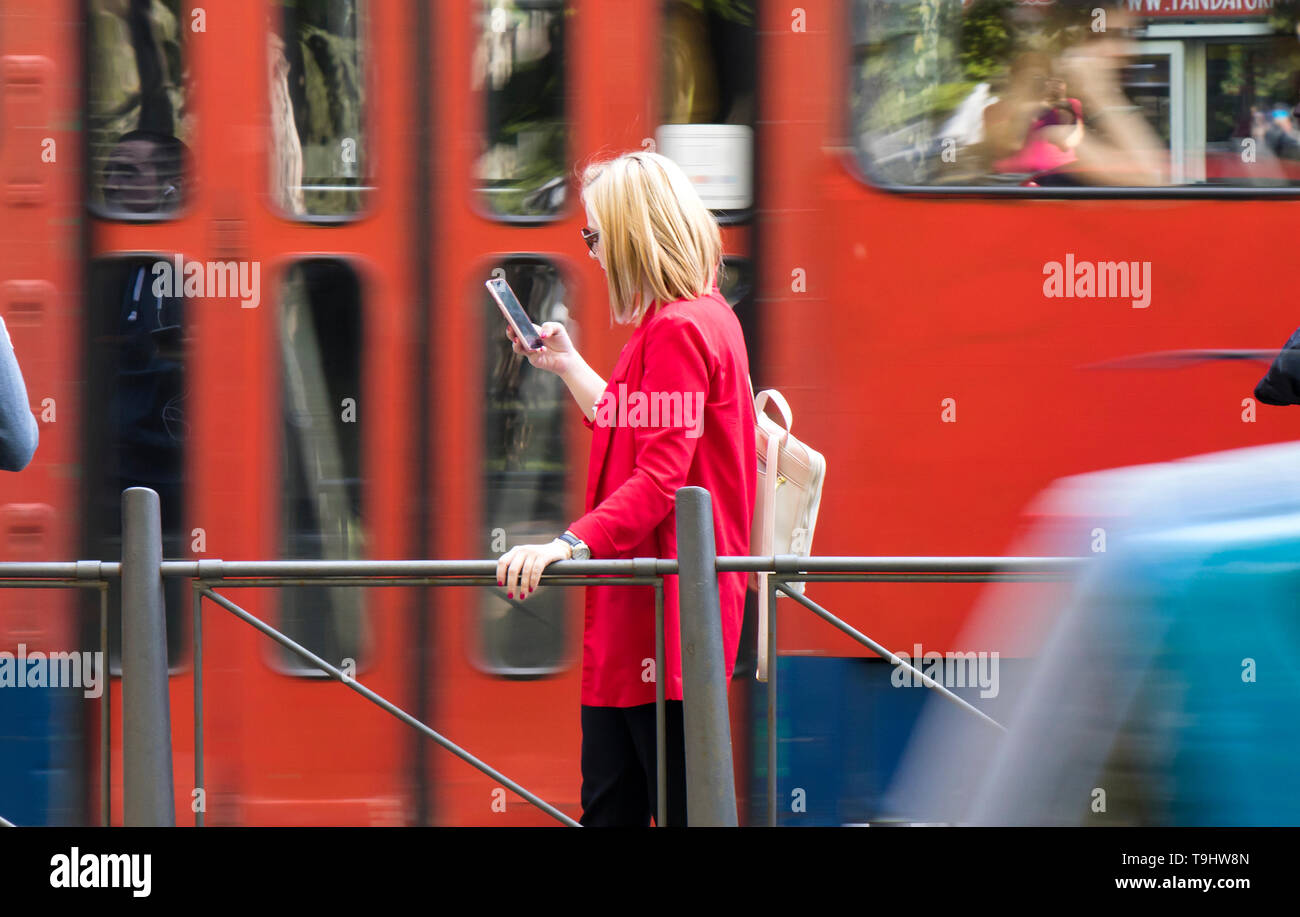 Belgrad, Serbien - April 22, 2019: junge blonde Frau an Ihr Mobiltelefon, während an der Bushaltestelle auf der Straße warten an einem sonnigen Frühlingstag mit Stockfoto