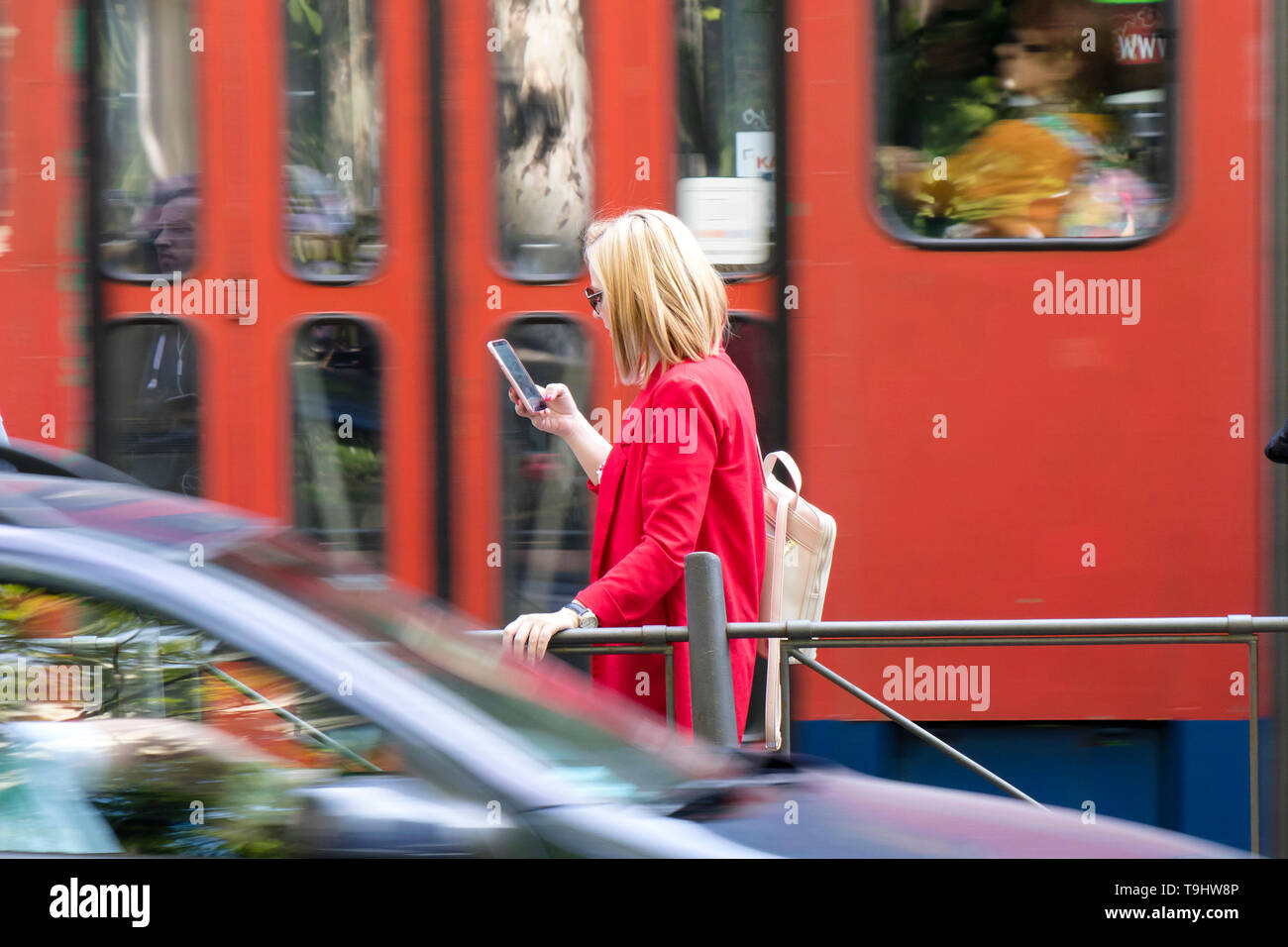 Belgrad, Serbien - April 22, 2019: junge blonde Frau an Ihr Mobiltelefon, während an der Bushaltestelle auf der Straße warten an einem sonnigen Frühlingstag mit Stockfoto