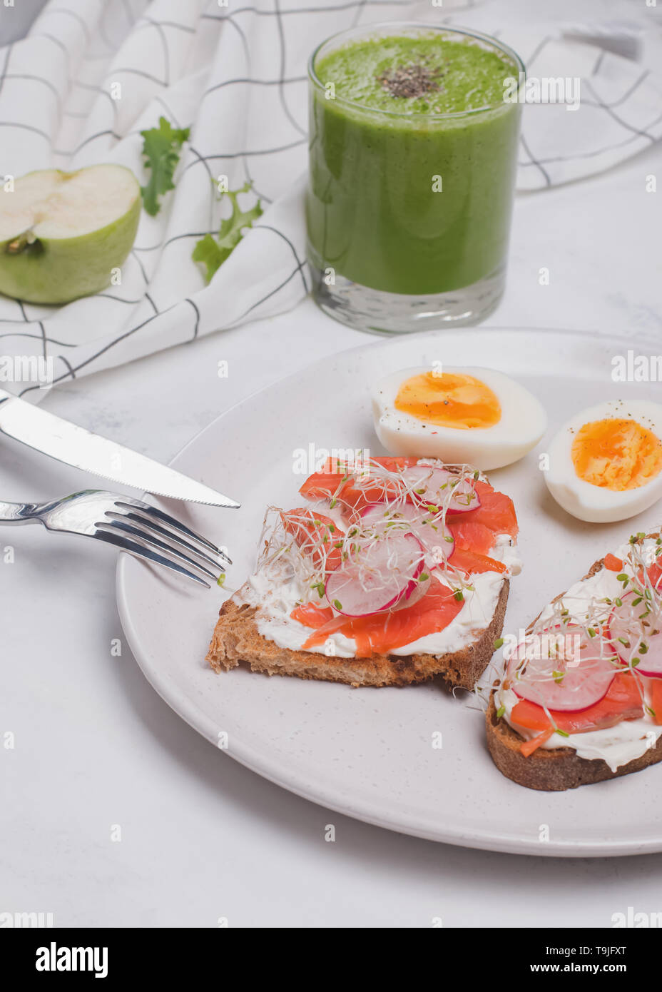 Toast mit Frischkäse und Lachs, hartgekochte Eier und grünen Smoothie. Gesundes Frühstück auf dem weißen Tisch Stockfoto