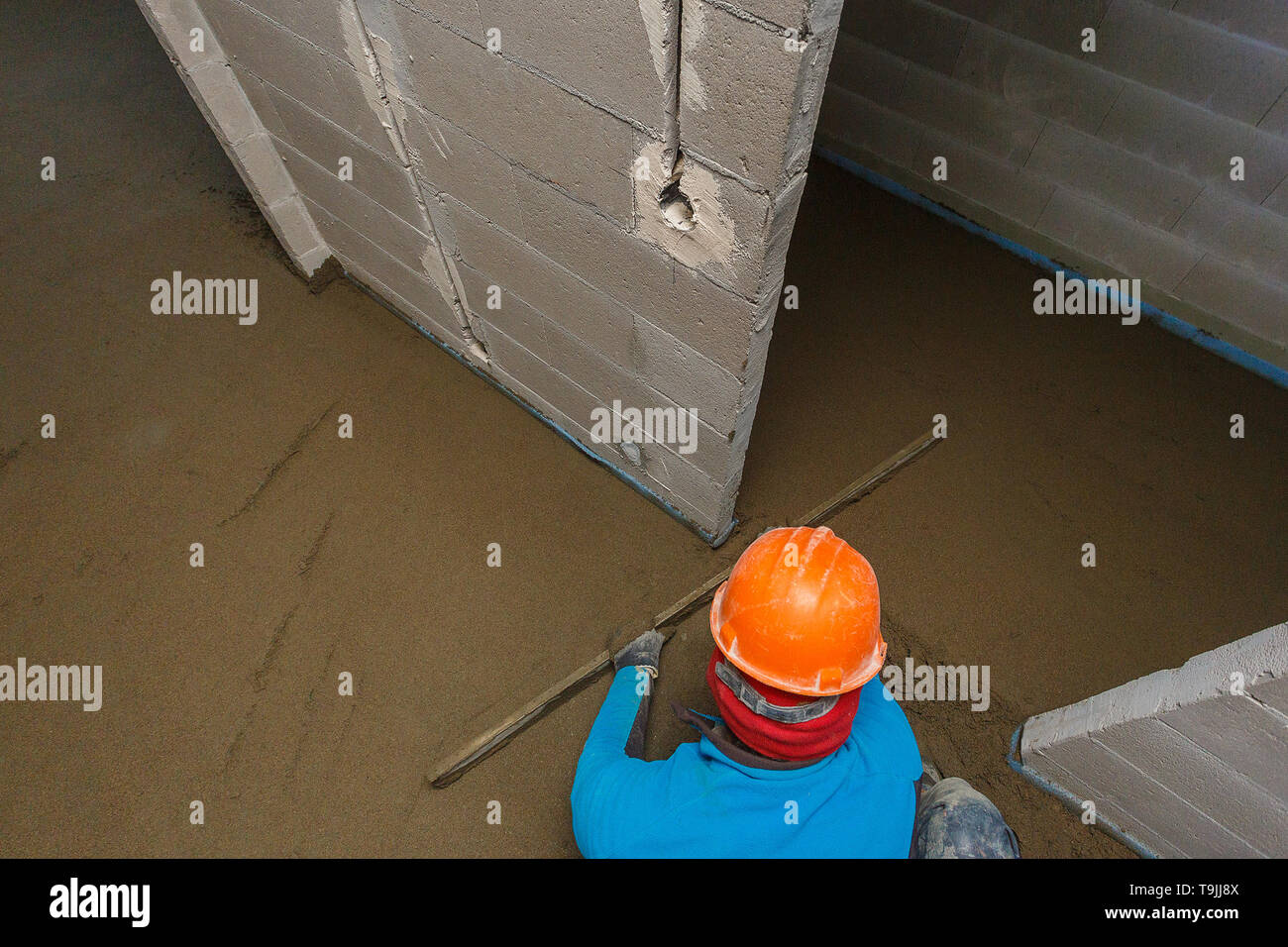 Der Arbeiter in einem orange Helm ist die Nivellierung der Estrich Lösung. Stockfoto