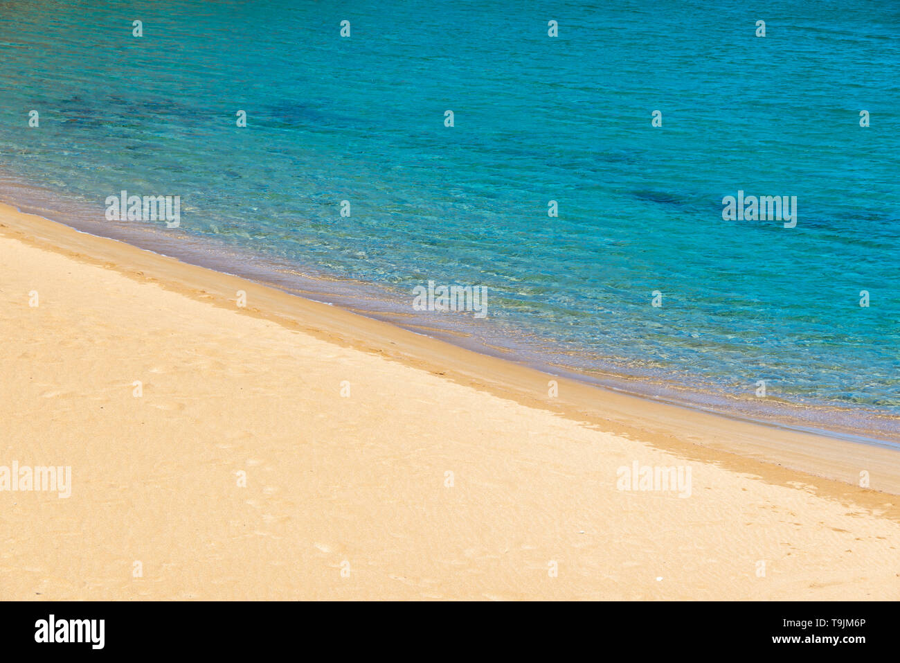 Strand mit orange Sand und blauem Wasser Stockfoto