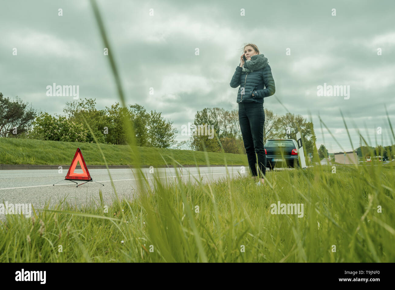 Eine junge Frau ist am Telefon mit einer Autopanne Stockfoto