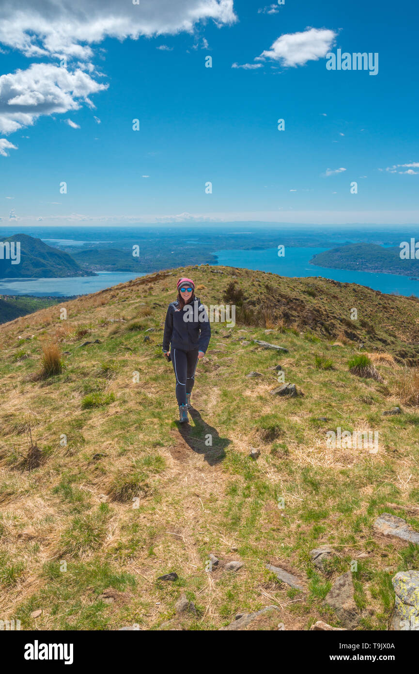 Gerne weibliche Wanderer mit Sonnenbrille zu Fuß auf einem Bergrücken. Herrliche Aussicht auf den Lago Maggiore. Lächelnde Mädchen Wandern Mountain Trail in Piemont, Italien. Stockfoto