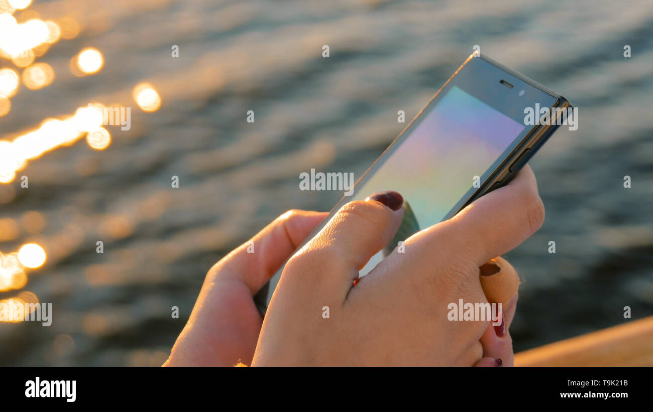 Frau mit Smartphone an Deck Kreuzfahrt Schiff bei Sonnenuntergang Stockfoto