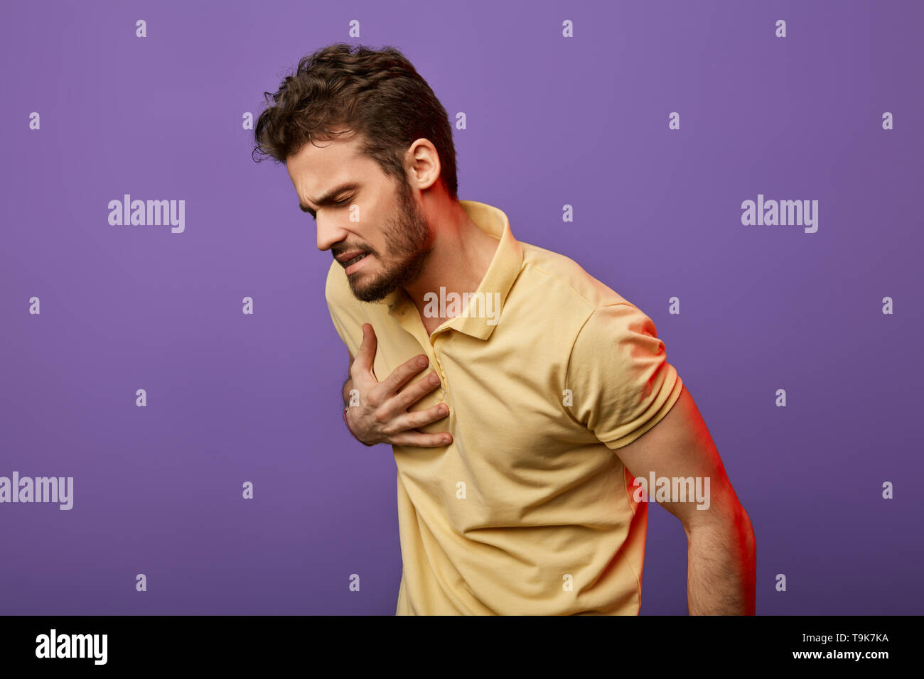 Schwachen kranken Kerl Probleme mit Herz. Attraktive unglücklichen Mann im gelben T-Shirt seine Brust berühren, Herzen. schließen Foto. Isolierte blauen Hintergrund. myokardiale infaction. Herzklopfen Stockfoto