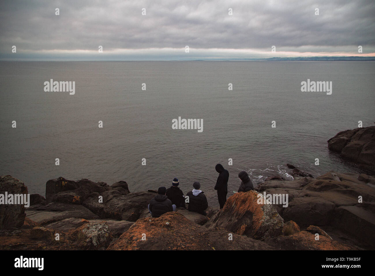 Freunde sitzen auf der Klippe am Meer auf trübe winter Morgen mit Blick auf das Meer Stockfoto