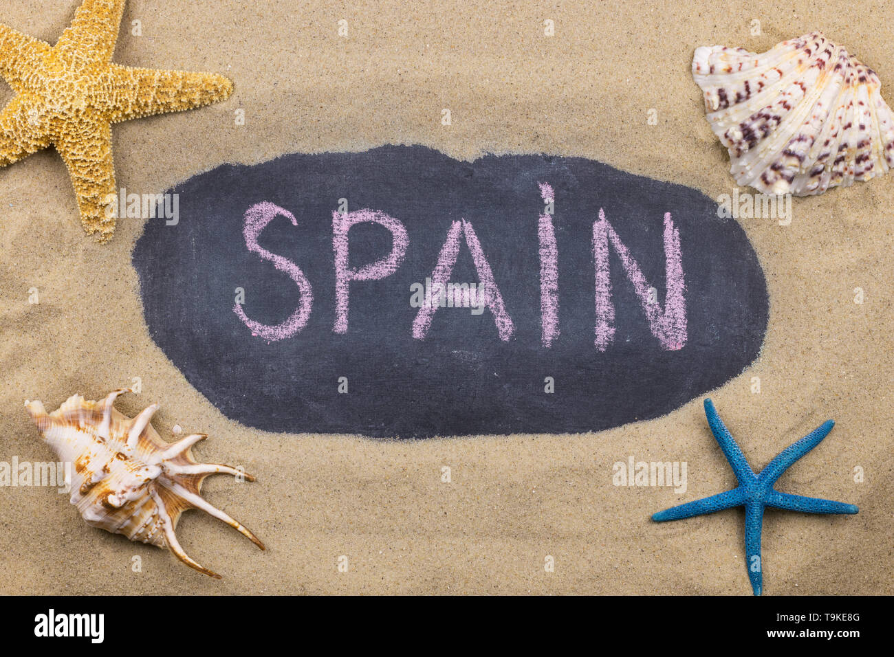 Handschriftliche Wort Spanien mit Kreide geschrieben, unter Muscheln und Seesterne. Ansicht von oben Stockfoto