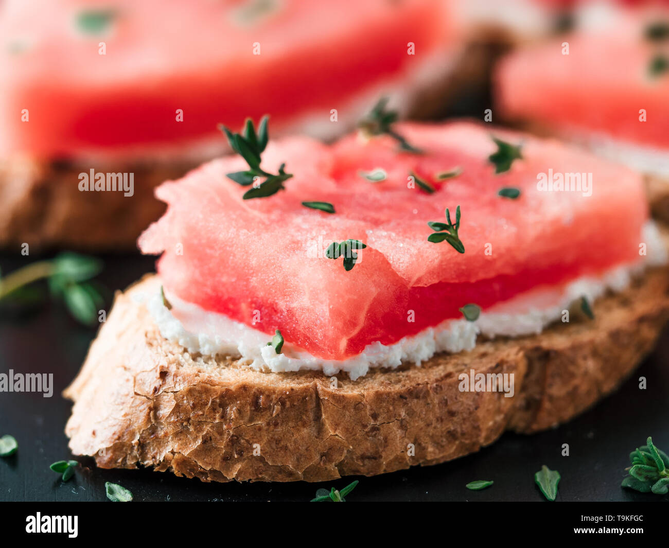 Toast mit Frischkäse, Wassermelone und frischem Thymian. Salzige käse, süßes Wassermelone und würziger Thymian auf knusprig gegrillte Brotscheiben. Idee und Rezept für ungewöhnliche gesundes Frühstück, Snacks und Mittagessen Stockfoto