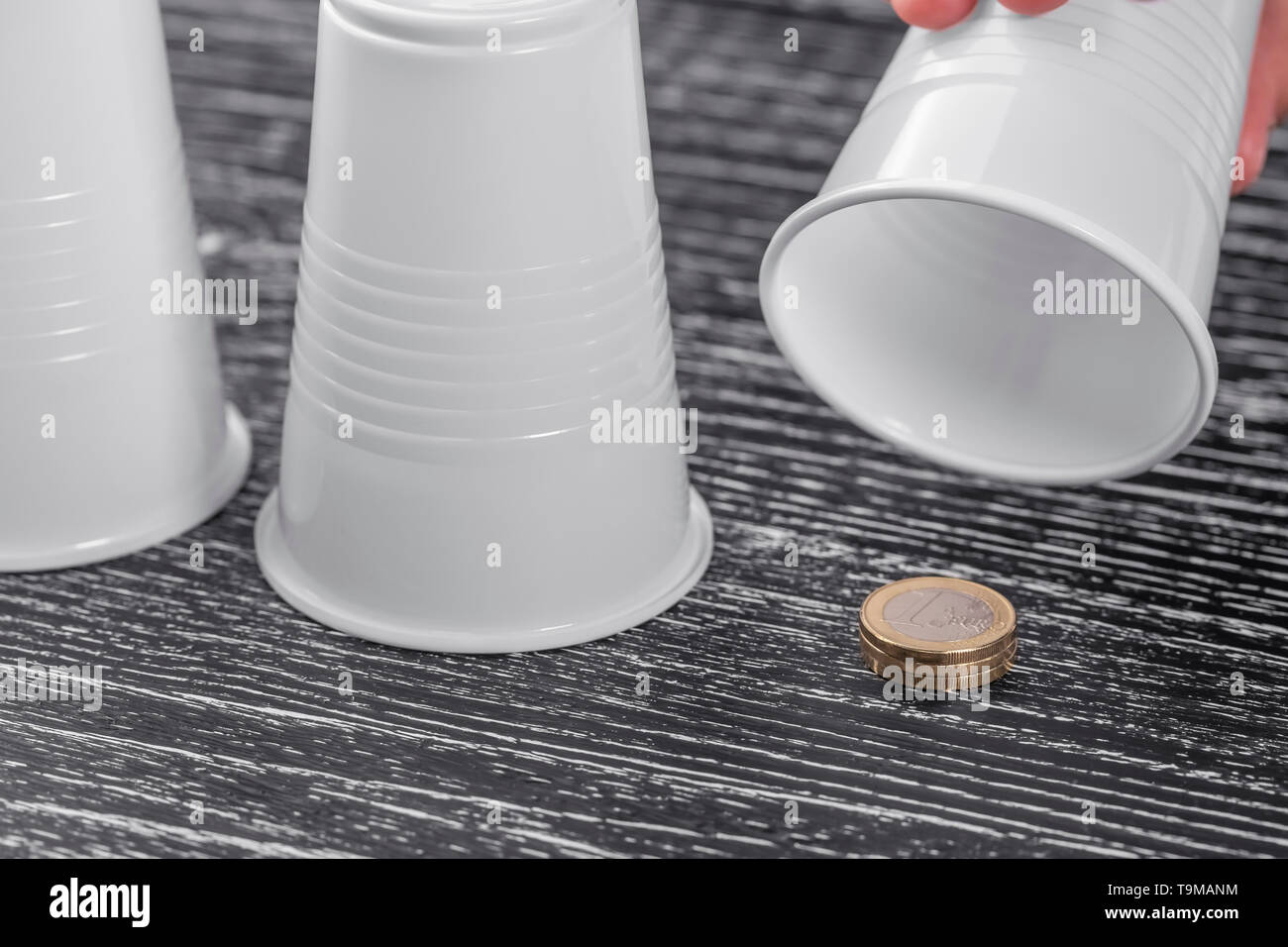 Preis unter einer von drei Plastikbecher in einer Shell Spiel auf einem schwarzen Holztisch. Münzen für 1 Euro. Symbol der monetären Sieg in Wetten Glücksspiel Stockfoto