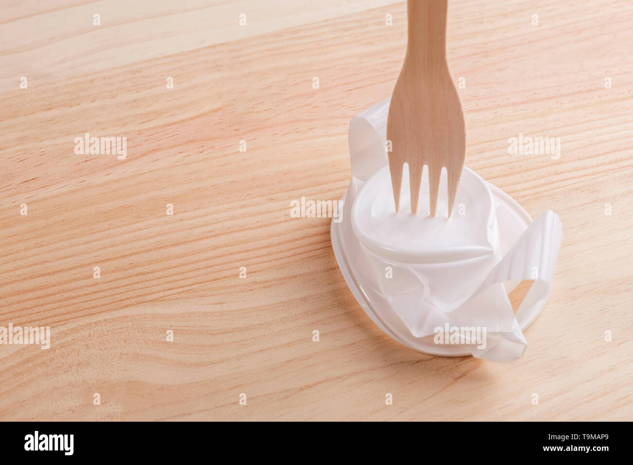 Weiße Schale aus Kunststoff mit einem hölzernen eco Gabel auf dem Holz Tisch zerknittert. Der Begriff der Exzellenz eco Produkte über Kunststoff Stockfoto