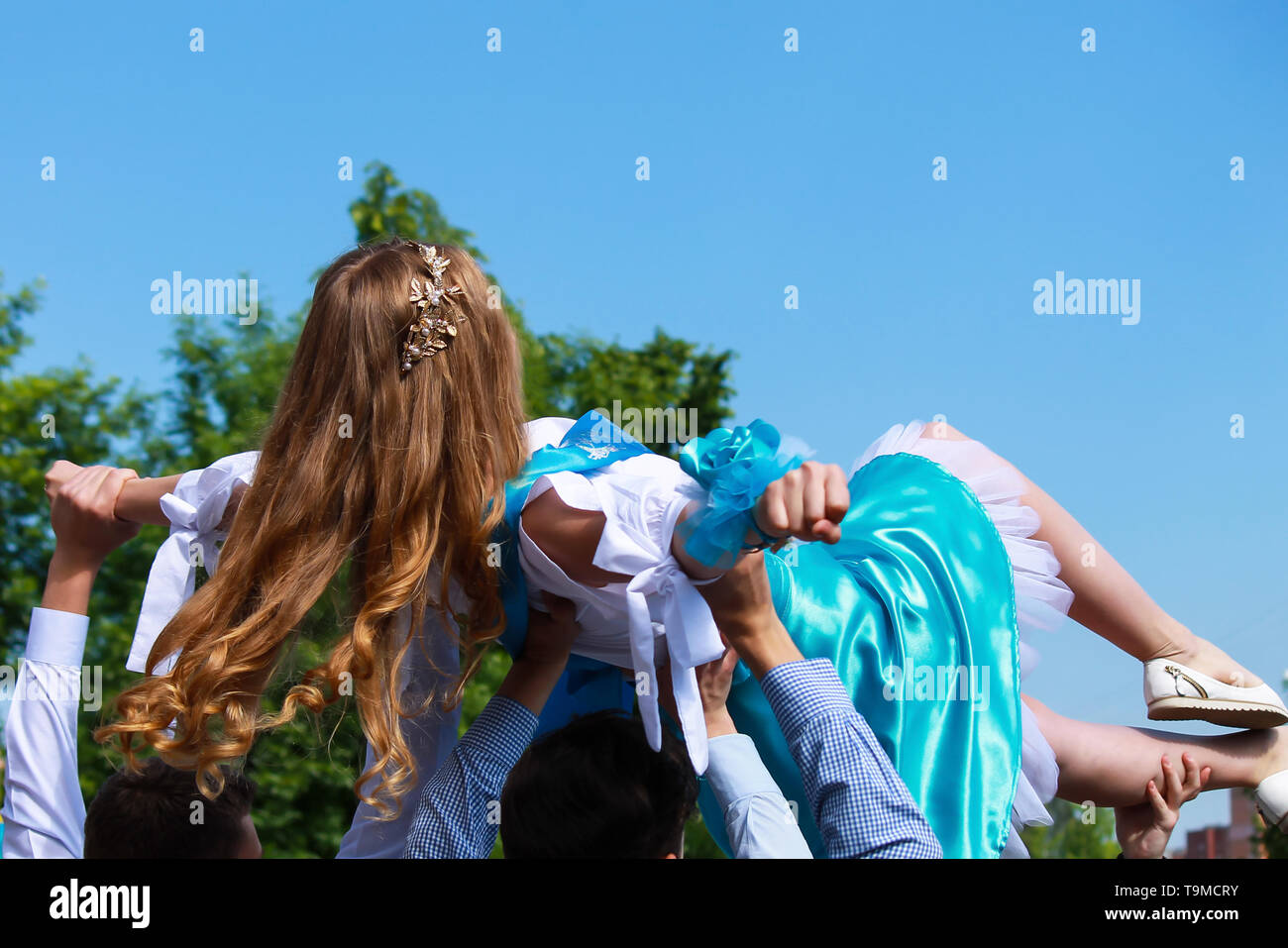 Das blonde Mädchen in der weiss-blauen Dress auf dem erhöhten männlichen Hände beim Tanzen. Hochzeit, Geburtstag, Staffelung. Urlaub, Frühling und Sommer Stockfoto