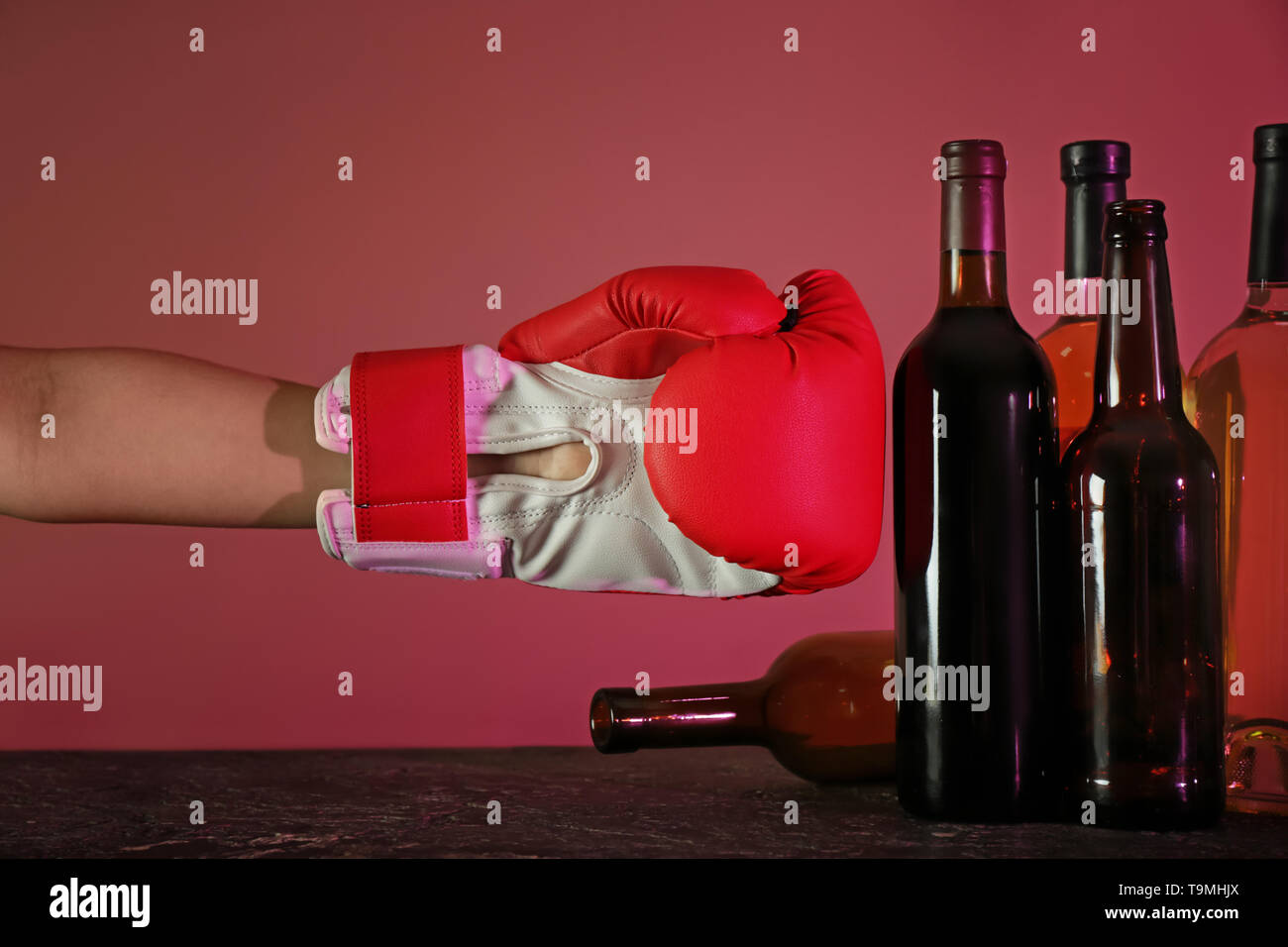 Hand tragen Boxhandschuh in der Nähe von Flaschen Wein. Konzept des Alkoholismus Stockfoto