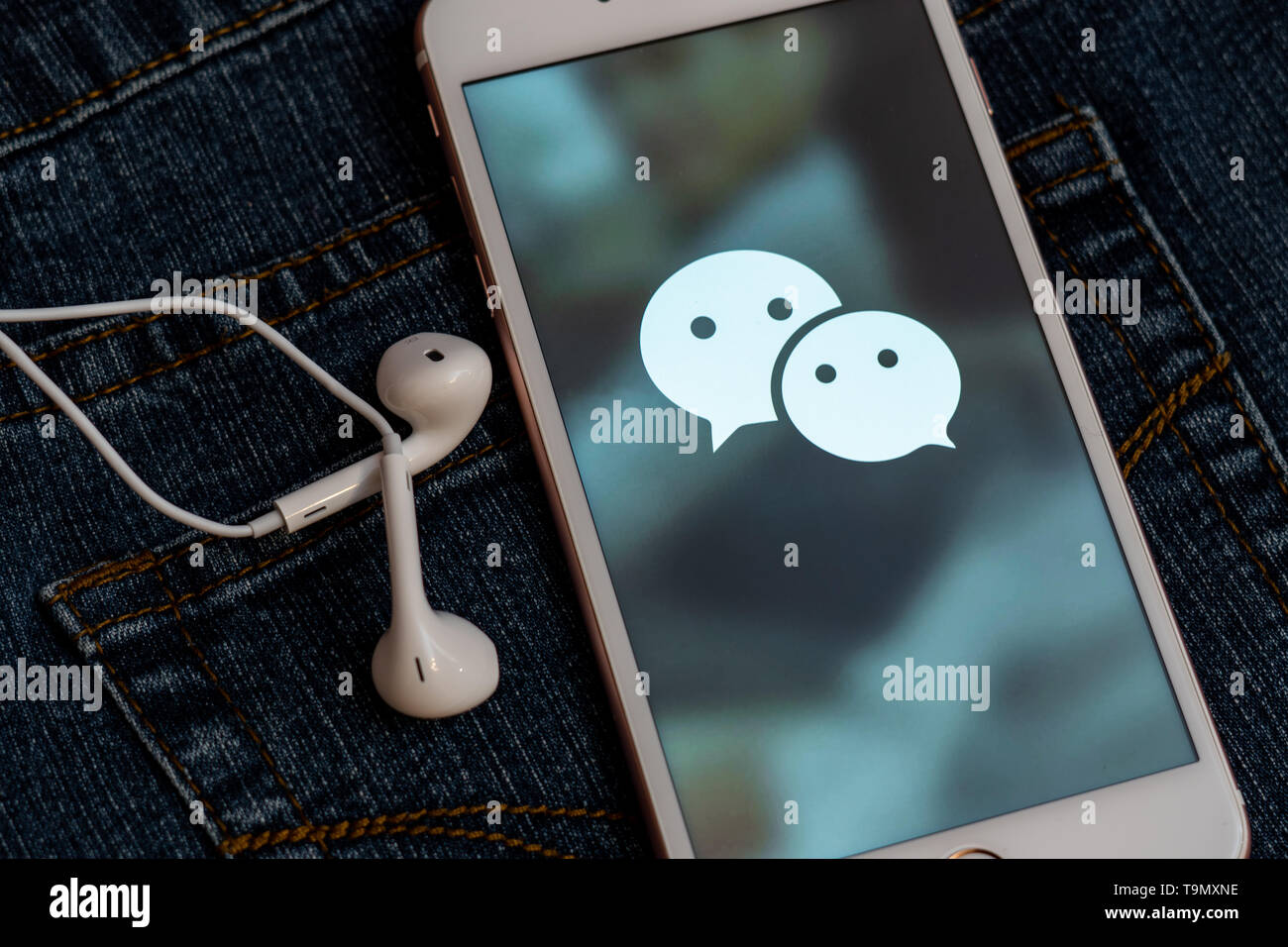 Weißes iPhone mit Logo von social media WeChat aus China auf dem Bildschirm. Social media Symbol. Denim Jeans Hintergrund. Marketing oder Business Konzept Stockfoto