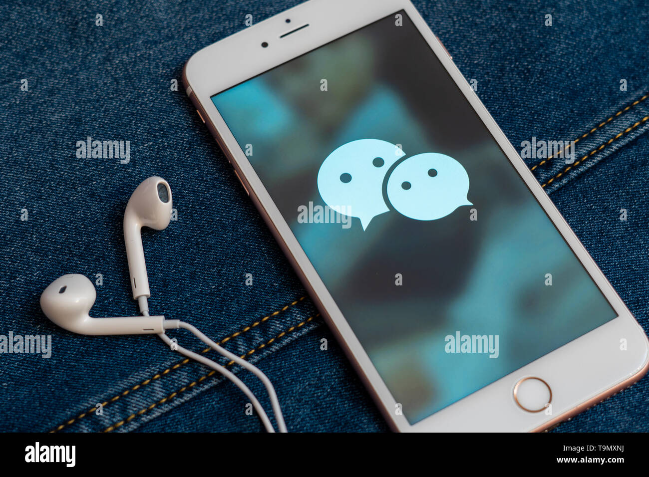 Weißes iPhone mit Logo von social media WeChat aus China auf dem Bildschirm. Social media Symbol. Denim Jeans Hintergrund. Marketing oder Business Konzept Stockfoto