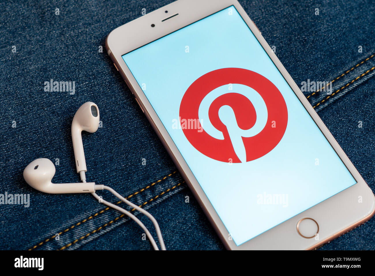 Weißes iPhone mit Logo von social media Pinterest auf dem Bildschirm. Social media Symbol. Denim Jeans Hintergrund. Marketing oder Business Konzept Stockfoto