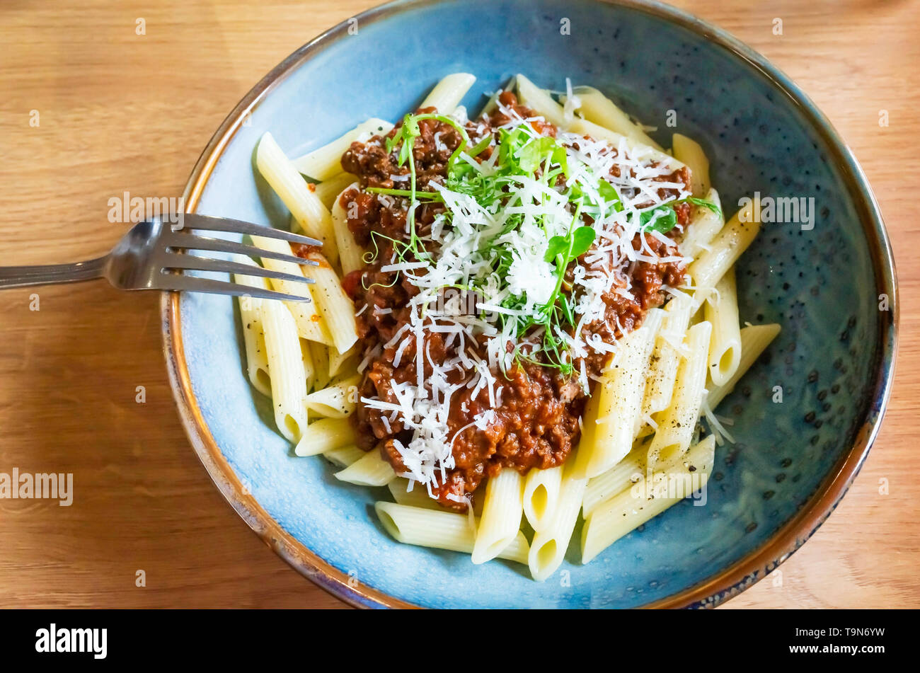 Restaurant Hauptgericht Nudeln Bolognese mit geriebenem Parmesan Salat garnieren und schwarzer Pfeffer in eine blaue Schale Stockfoto