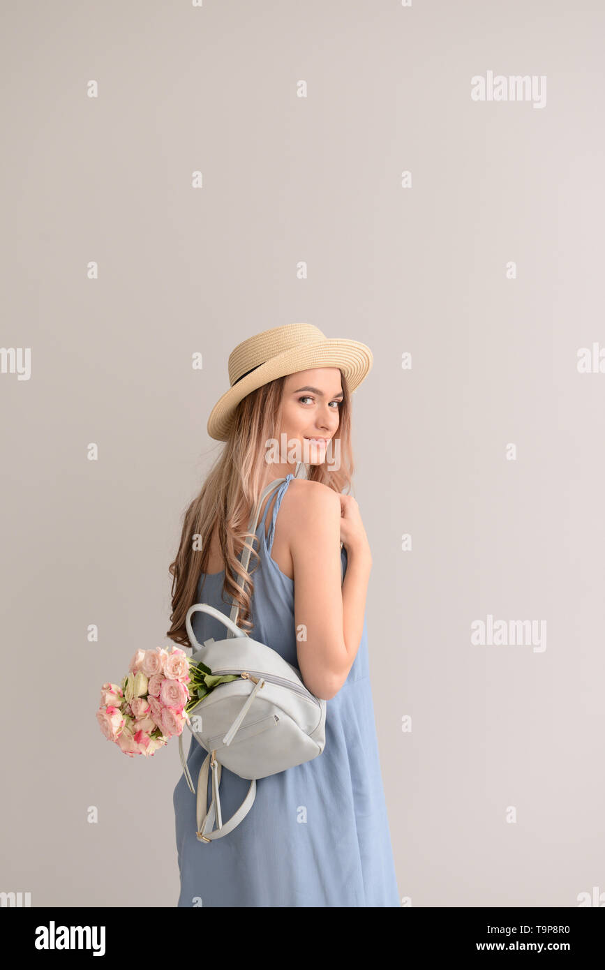 Schöne junge Frau mit Blumenstrauß und Rucksack auf grauem Hintergrund Stockfoto