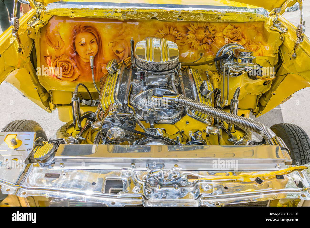 Ein Blick auf die verchromt und lackiert Motorraum, einschließlich von Hand gemalt von Frau Porträt und Blumen, auf eine helle gelbe Chevrolet lowrider Auto t Stockfoto