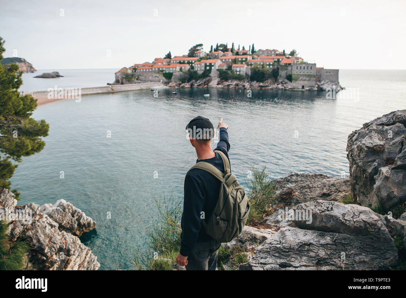 Touristen mit einem Rucksack in der Nähe des Meeres. Er zeigt seine Hand auf der Insel Sveti Stefan in Montenegro. Stockfoto