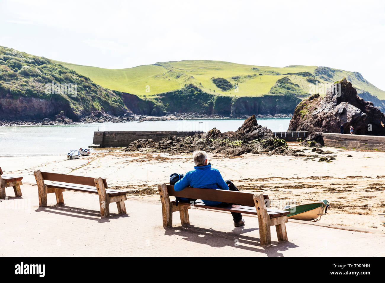 Hope Cove, Devon, UK, England, Hope Cove Devon, Mann aufs Meer suchen, sitzt auf der Bank, lehnte sich auf der Werkbank, mit Blick auf das Meer, Genießen, Entspannen, Stockfoto