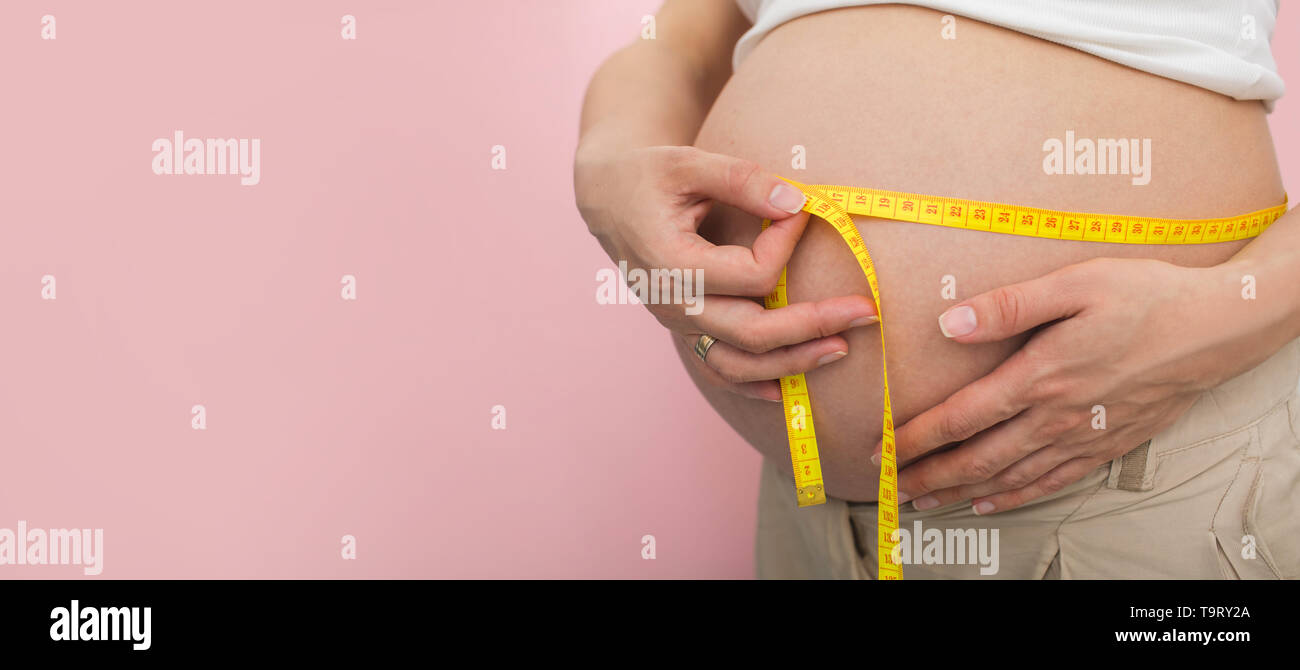 Schwangere Frau mit Messung Klebeband ihr Magen Messen auf rosa Hintergrund Stockfoto