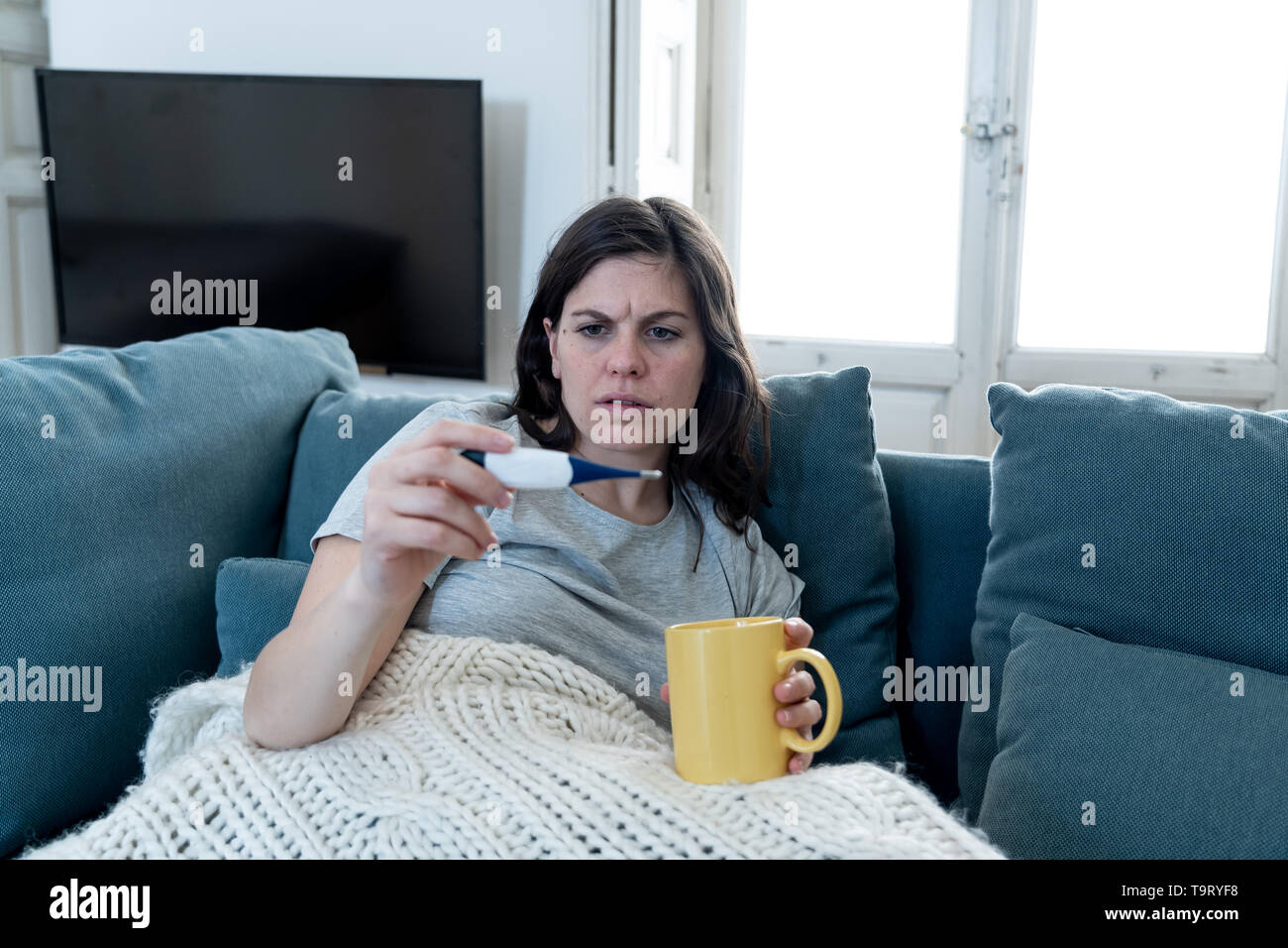Gesundheit und Medizin. Kranke Frau zu Hause auf dem Sofa liegend mit Kopfschmerzen Wunde Nase Kontrolle hoher Temperatur mit Thermometer Unwohlsein Müdigkeit ein Stockfoto